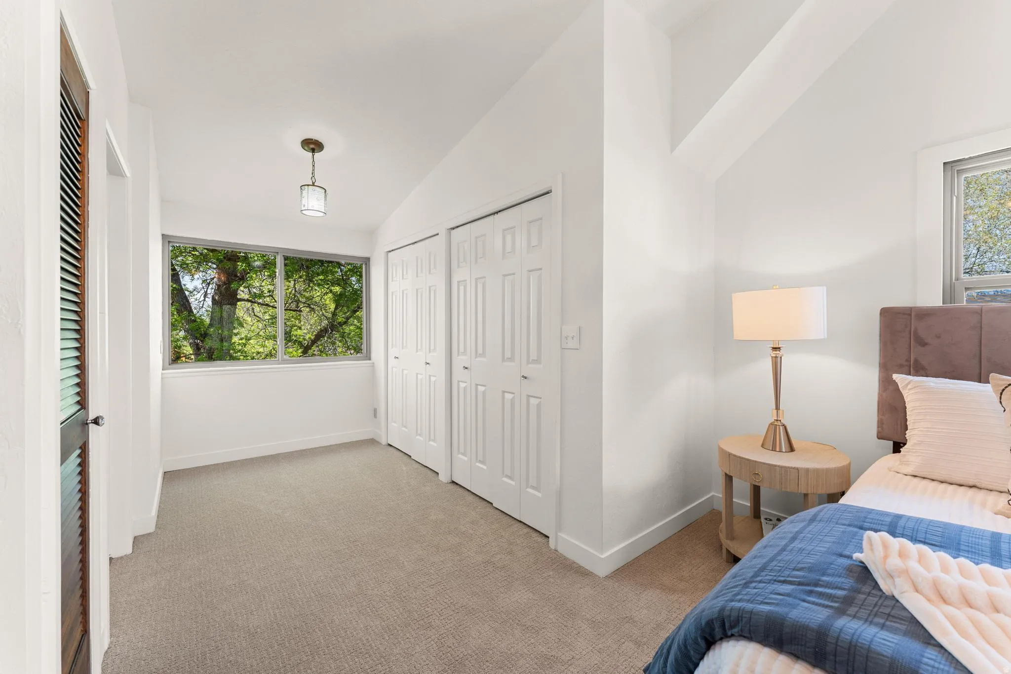Bedroom featuring vaulted ceiling, light colored carpet, and two closets