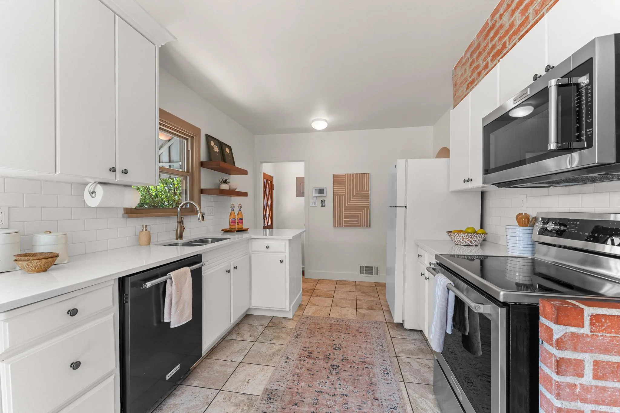 Kitchen with stainless steel appliances, white cabinetry, backsplash, open shelves, and light stone countertops