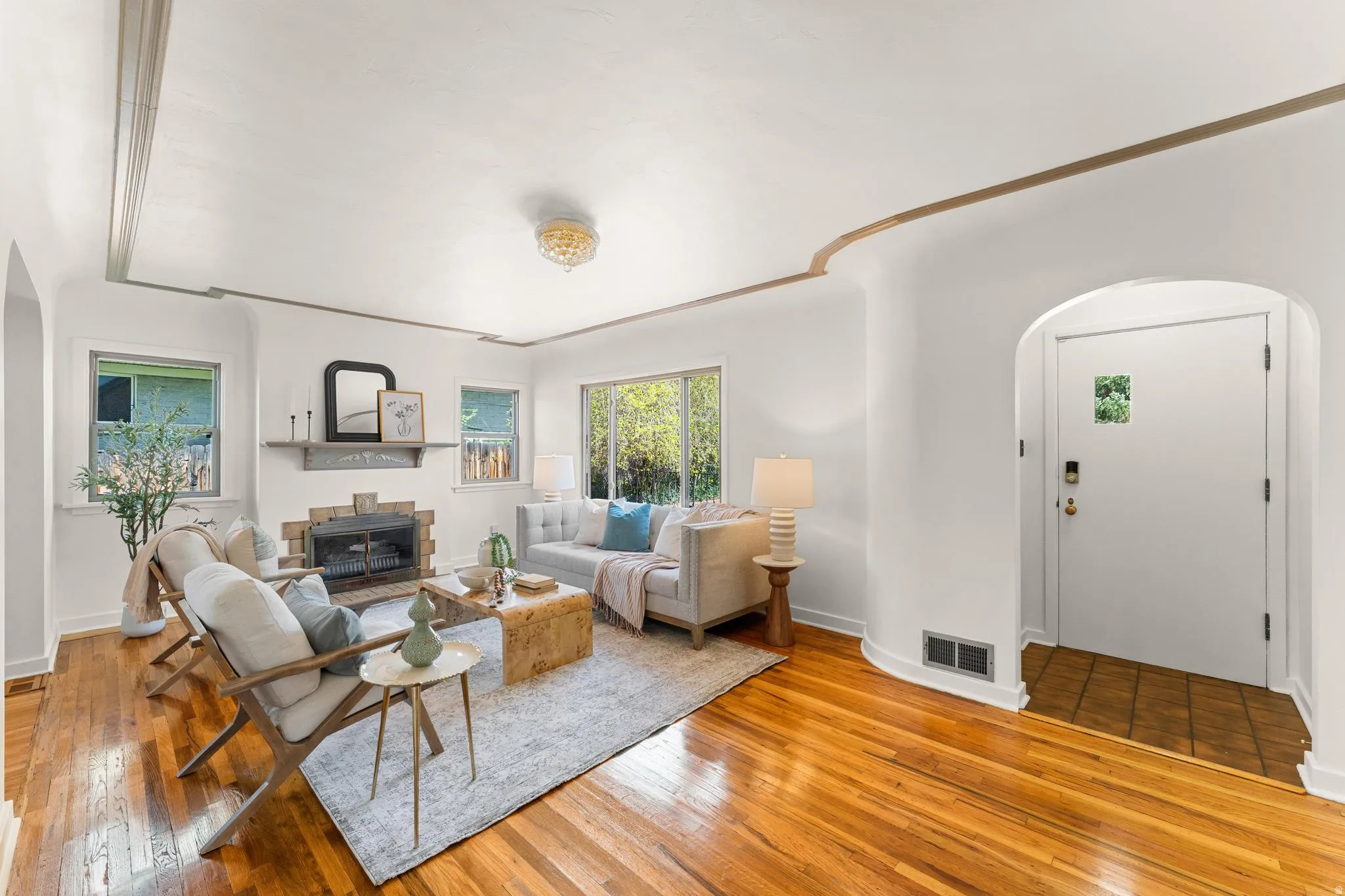 Living room featuring arched walkways, light wood finished floors, a glass covered fireplace, and crown molding