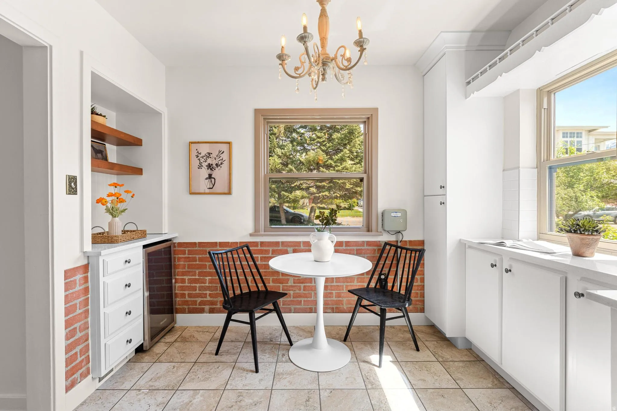 Dining space with breakfast area, a chandelier, beverage cooler, light tile patterned floors, and brick wall
