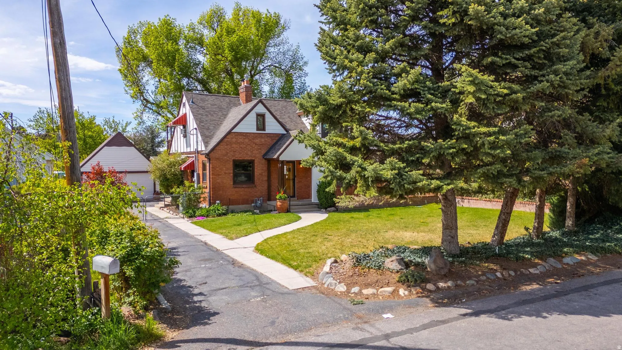 View of front facade featuring a front lawn, brick siding, a chimney, an outbuilding, and a detached garage