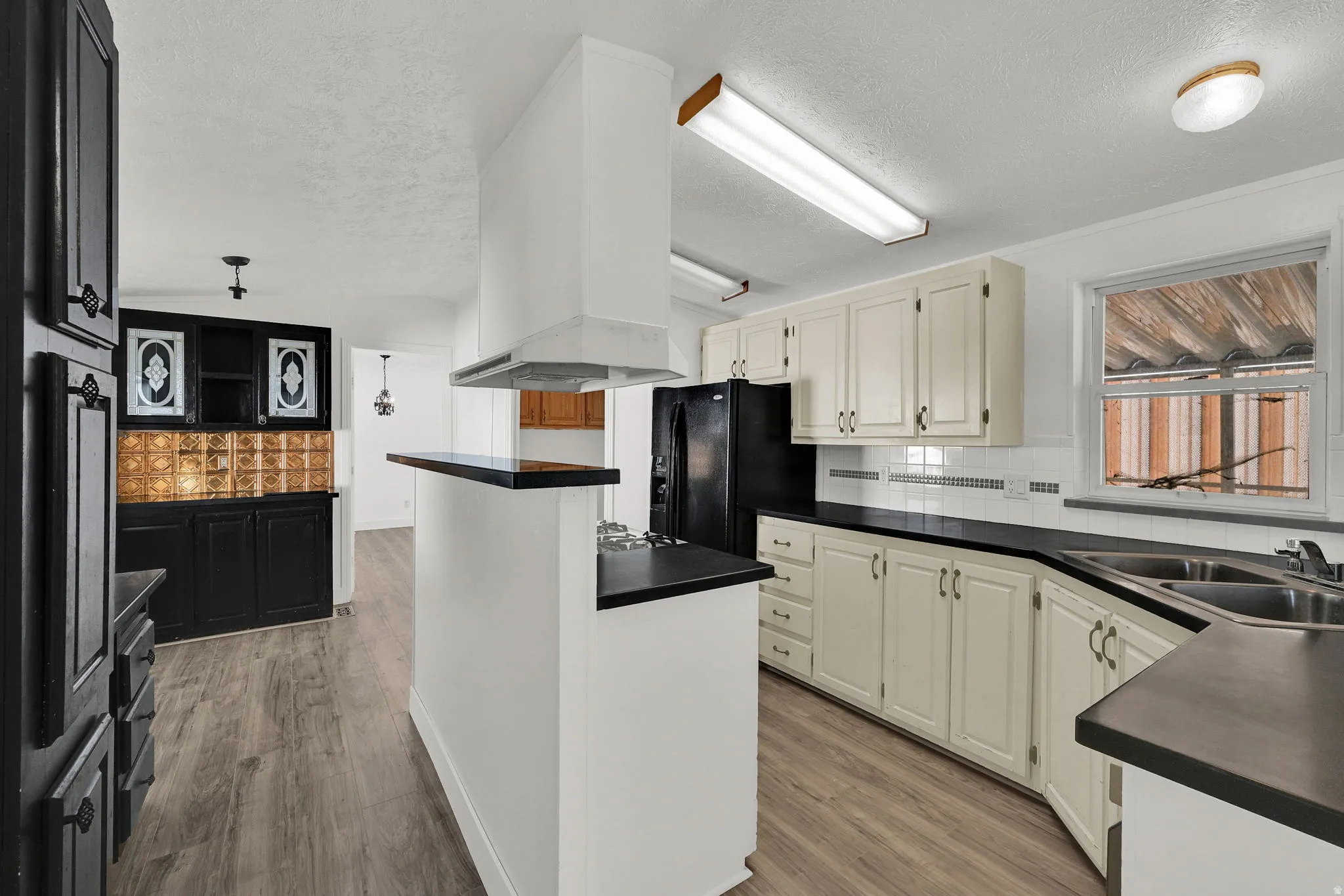 Kitchen with dark countertops, backsplash, a textured ceiling, light wood finished floors, and black fridge with ice dispenser