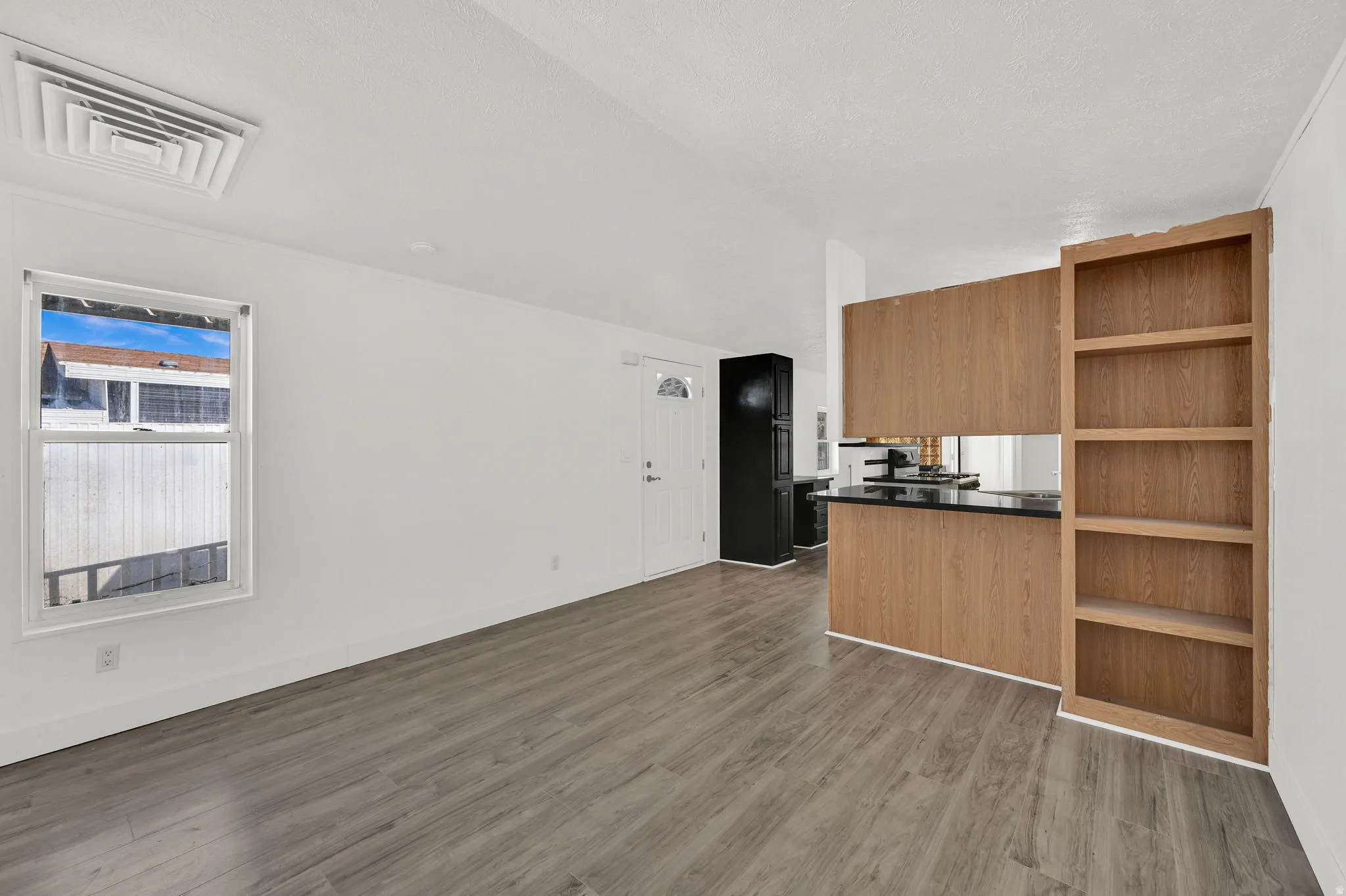 Kitchen featuring dark countertops, open shelves, wood finish cabinetry, dark wood-style flooring, and open floor plan