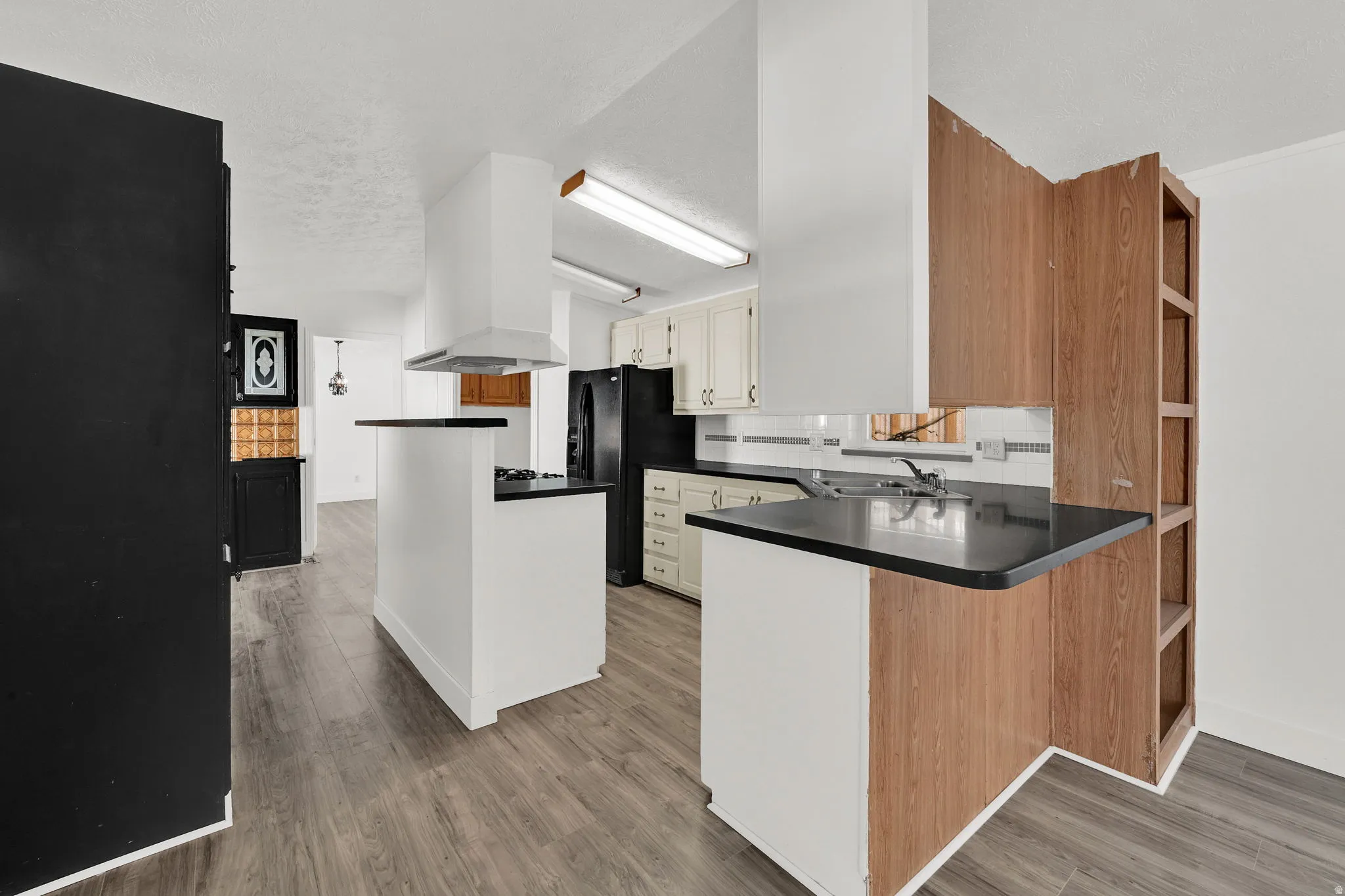 Kitchen featuring open shelves, a peninsula, dark countertops, and black fridge with ice dispenser