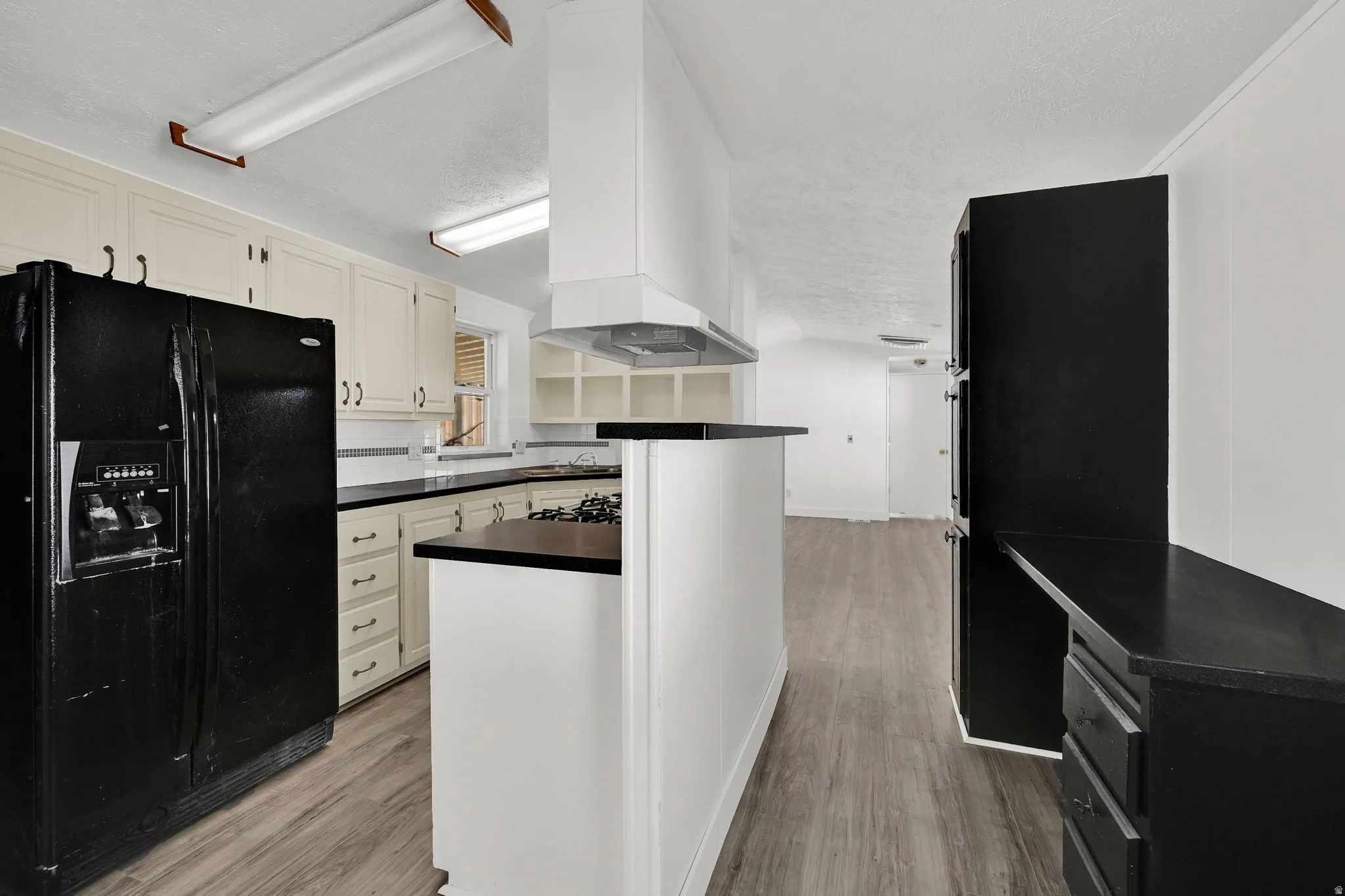 Kitchen featuring black fridge with ice dispenser, dark countertops, light wood-type flooring, a textured ceiling, and white cabinets