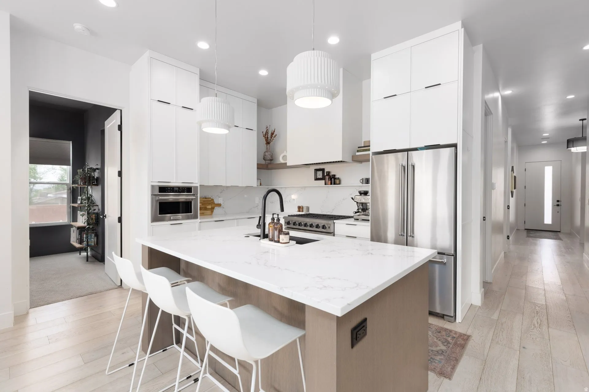 Kitchen with hanging light fixtures, premium appliances, light wood finished floors, light stone counters, and two tone cabinets