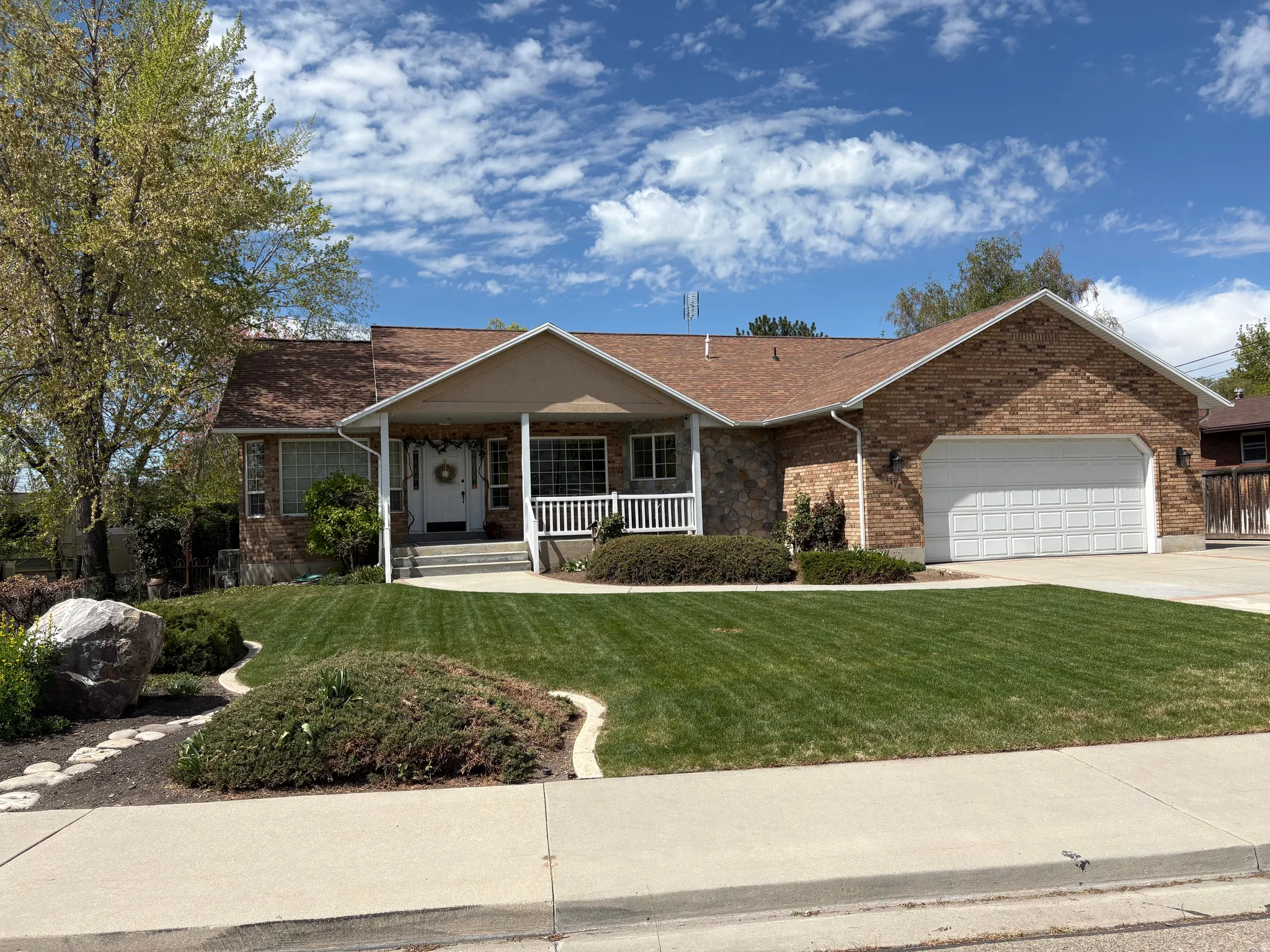 Ranch-style house featuring a front yard, covered porch, an attached garage, concrete driveway, and brick siding