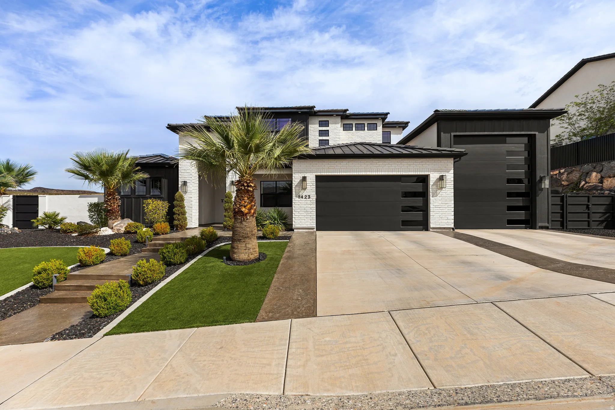 View of front of house with a standing seam roof, an attached garage, driveway, brick siding, and a front lawn