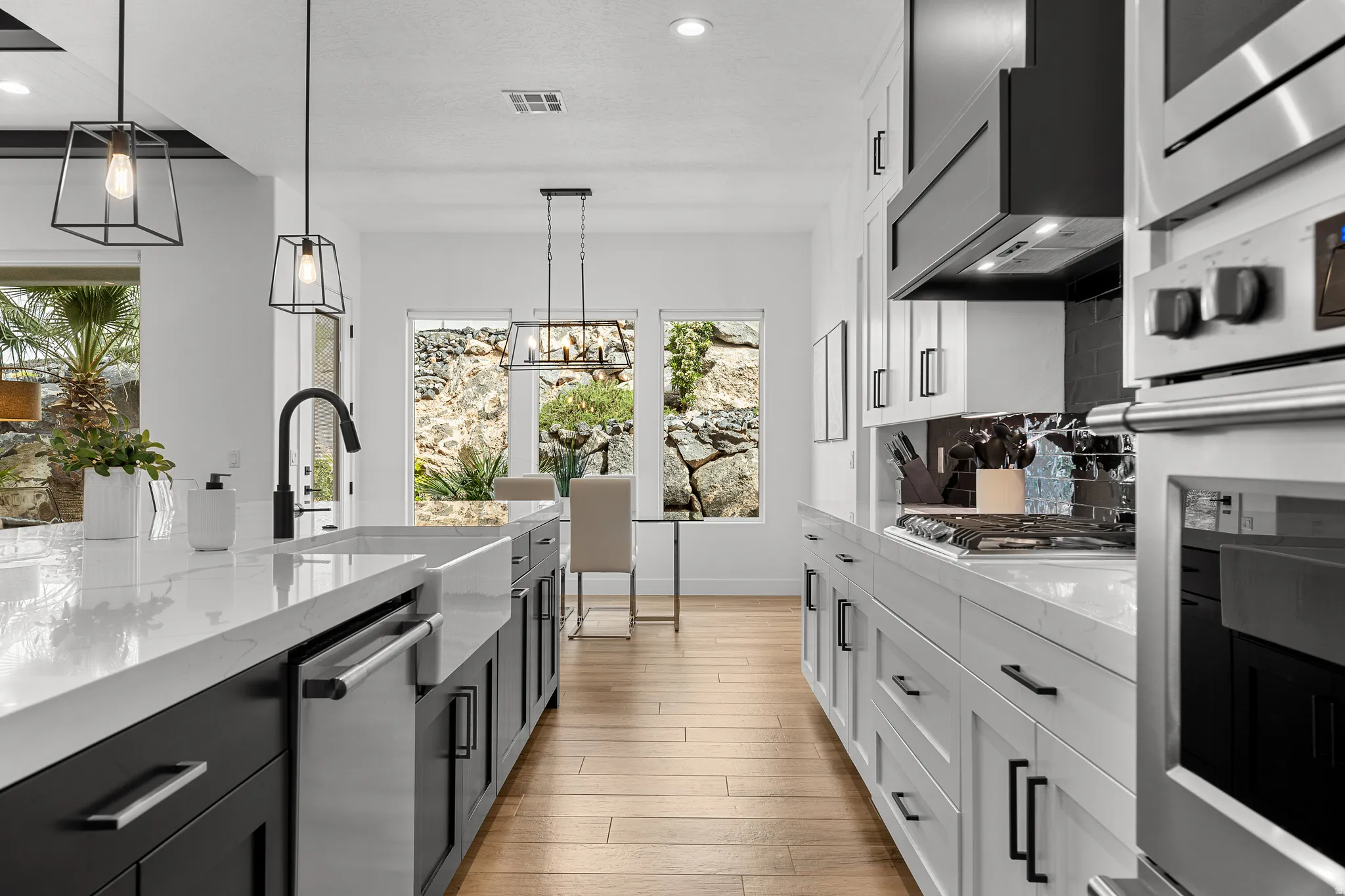 Two tone kitchen featuring dual tone cabinetry, stainless steel appliances, light stone countertops, light wood finished floors, and backsplash