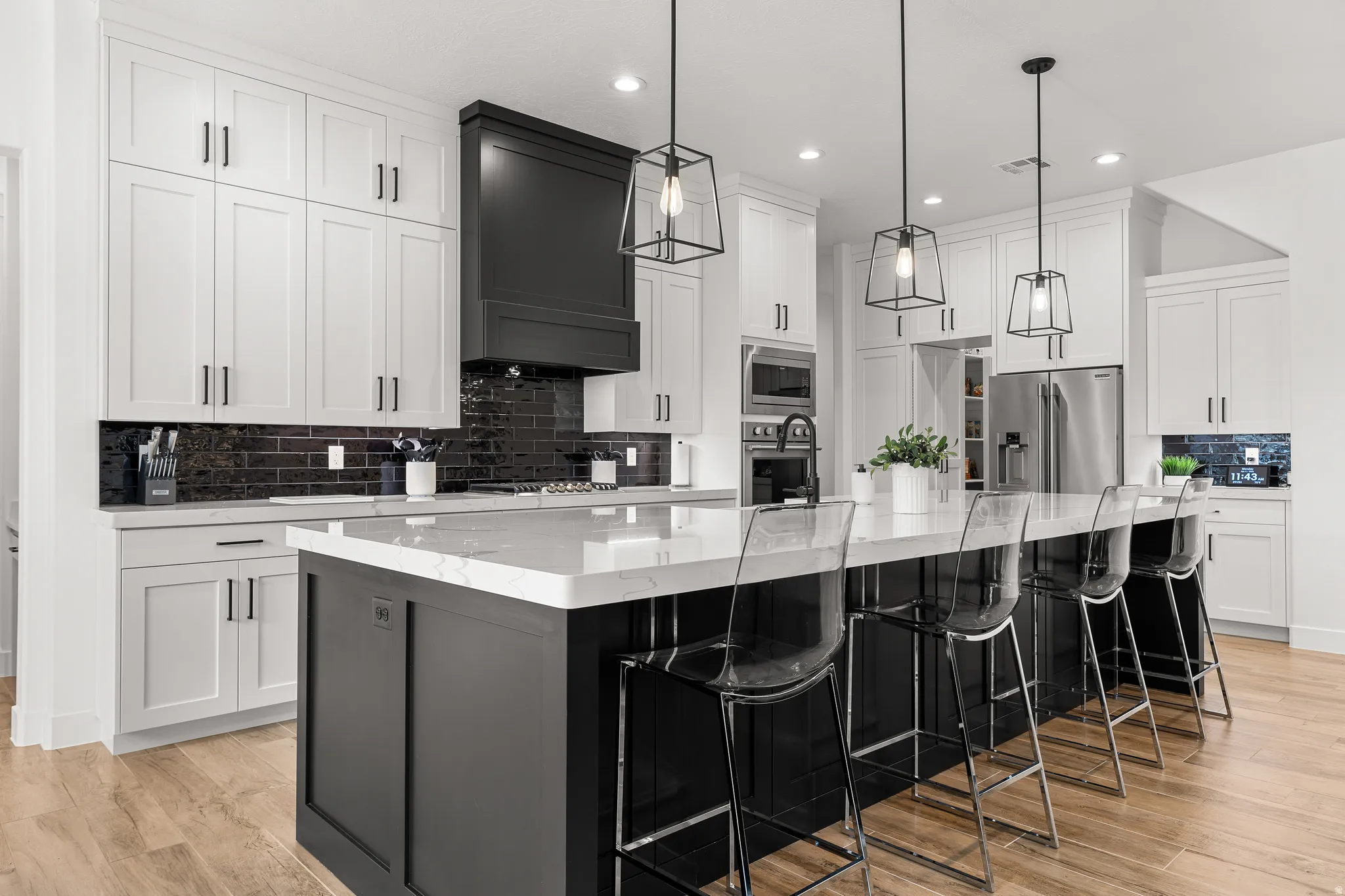 Two tone kitchen with decorative backsplash, a large island, two tone cabinets, stainless steel appliances, and light wood-style flooring