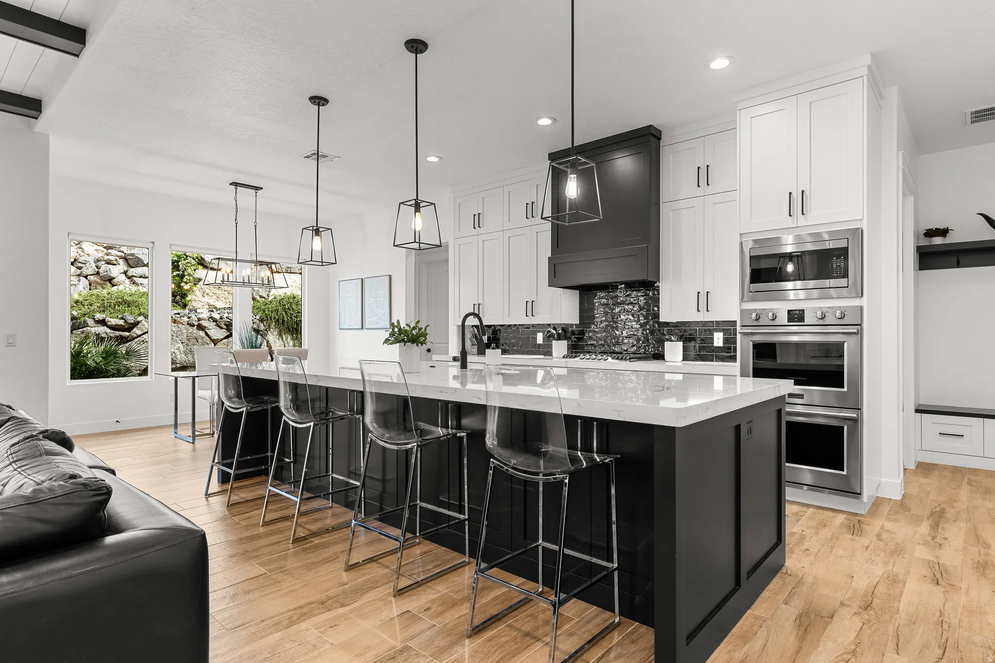 Two tone kitchen with stainless steel appliances, a breakfast bar area, light wood-style flooring, a large island with sink, and light stone counters
