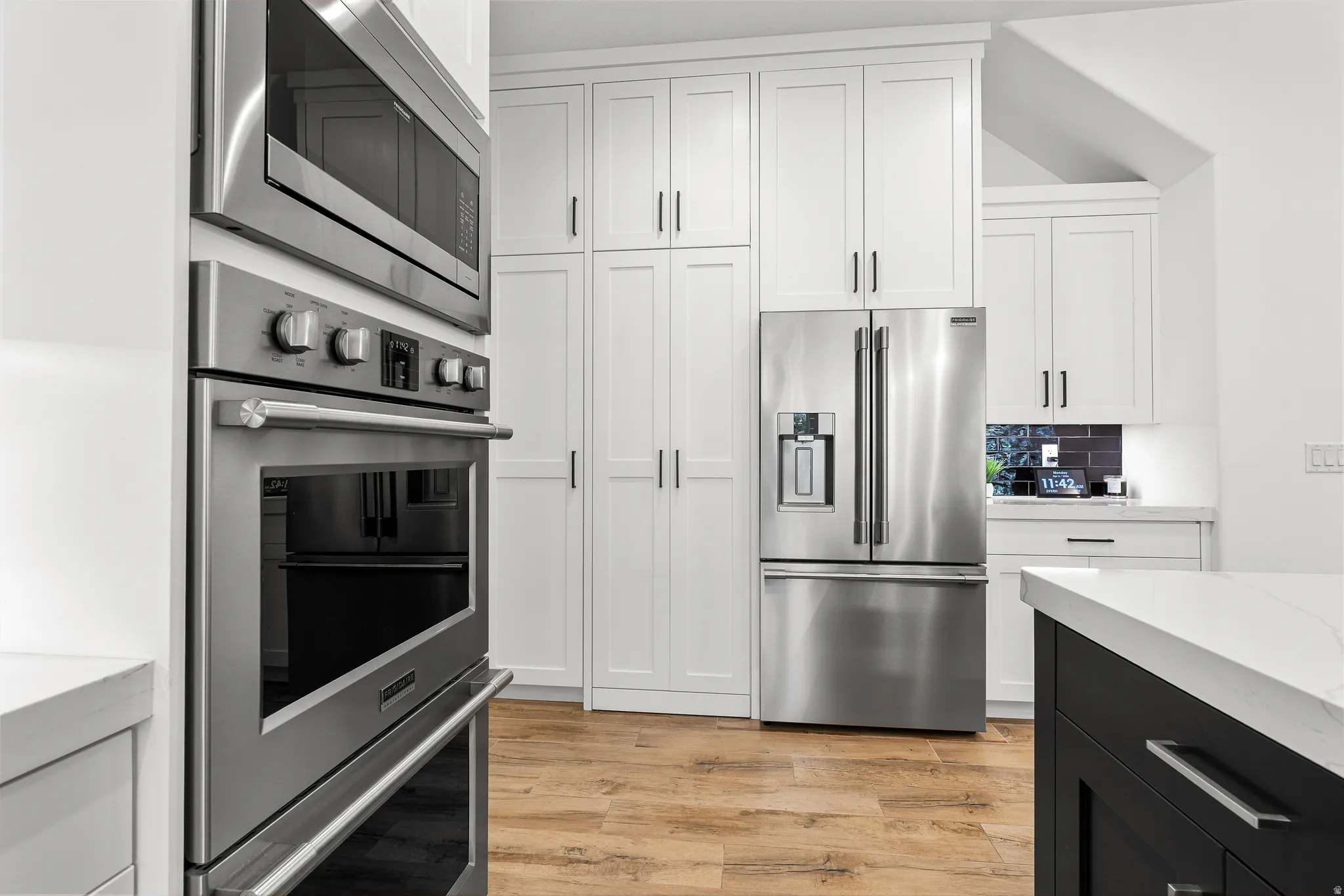 Kitchen with stainless steel appliances, light stone counters, two tone color scheme, and light wood-type flooring