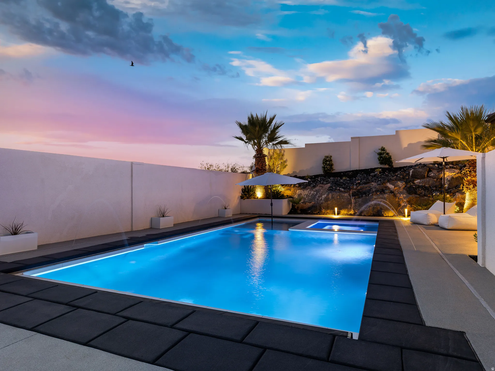 Pool at dusk with a fenced backyard, a patio area, and a pool with connected hot tub