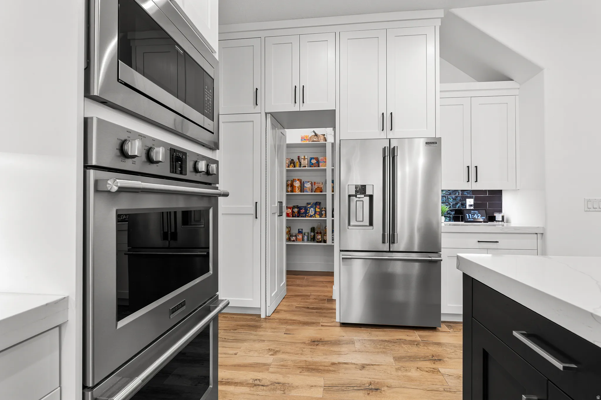 Kitchen with stainless steel appliances, light stone counters, two tone cabinetry, light wood-style flooring, and backsplash