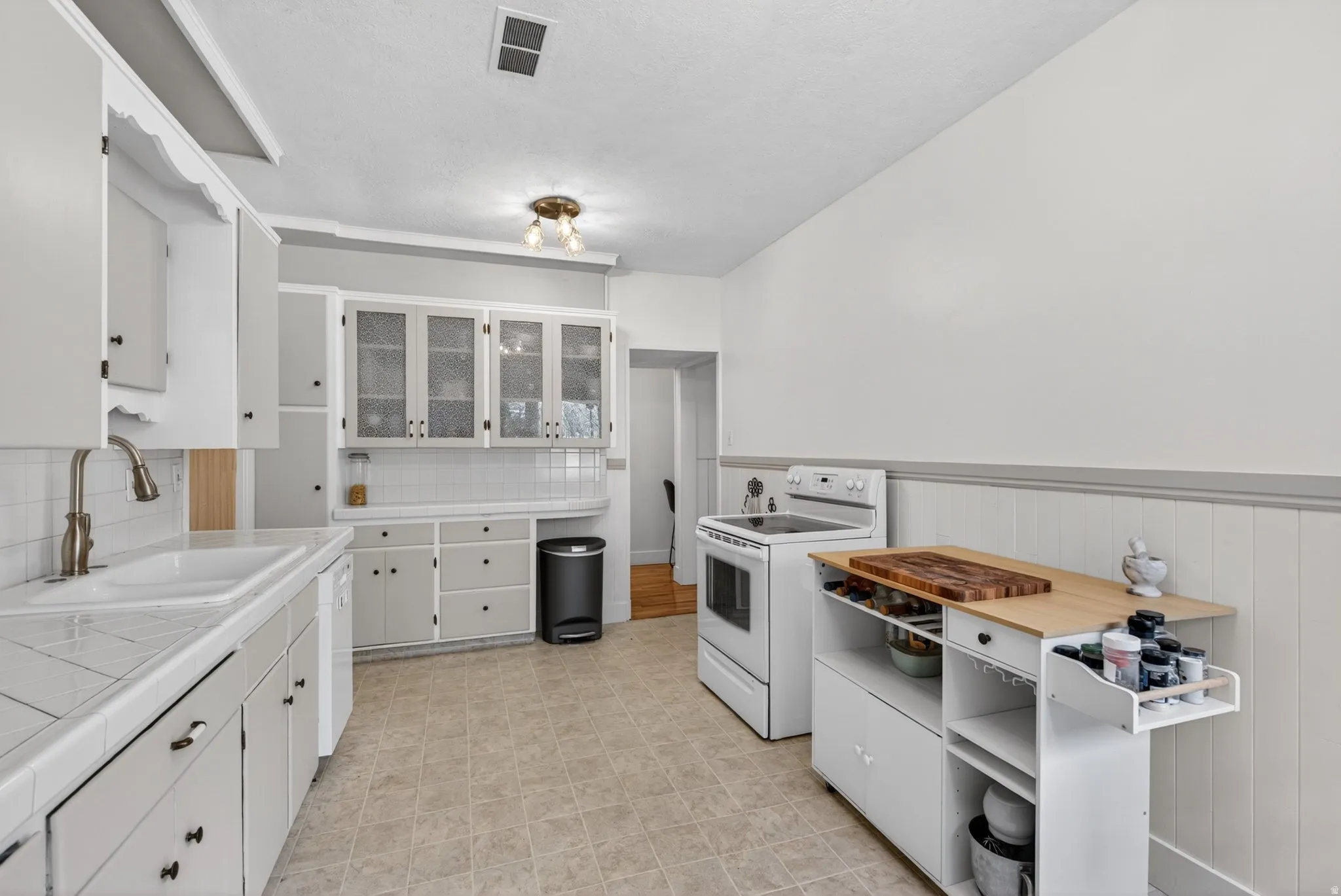 Kitchen featuring tile counters, white cabinetry, white appliances, and a wainscoted wall