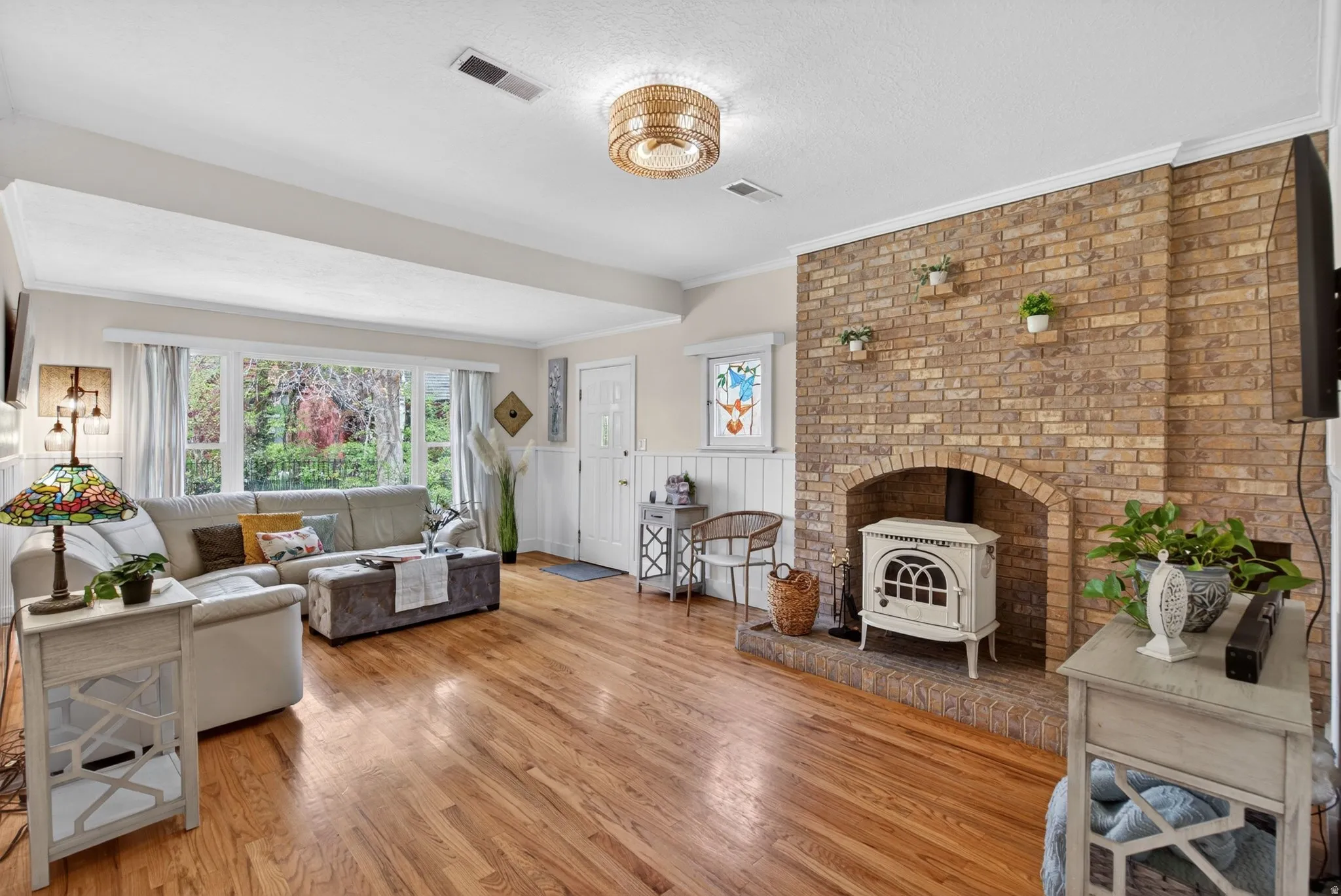 Living room with a wood stove, ornamental molding, light wood-style floors, a wainscoted wall, and a textured ceiling