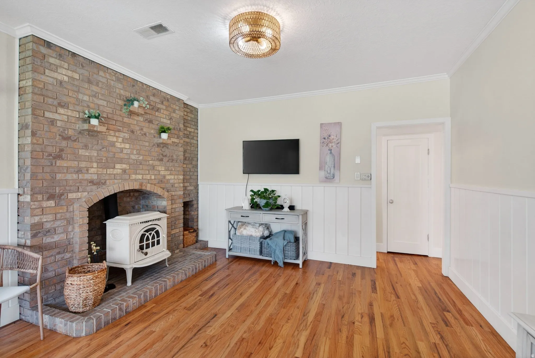 Living room with crown molding, light wood-style floors, a wainscoted wall, and a wood stove