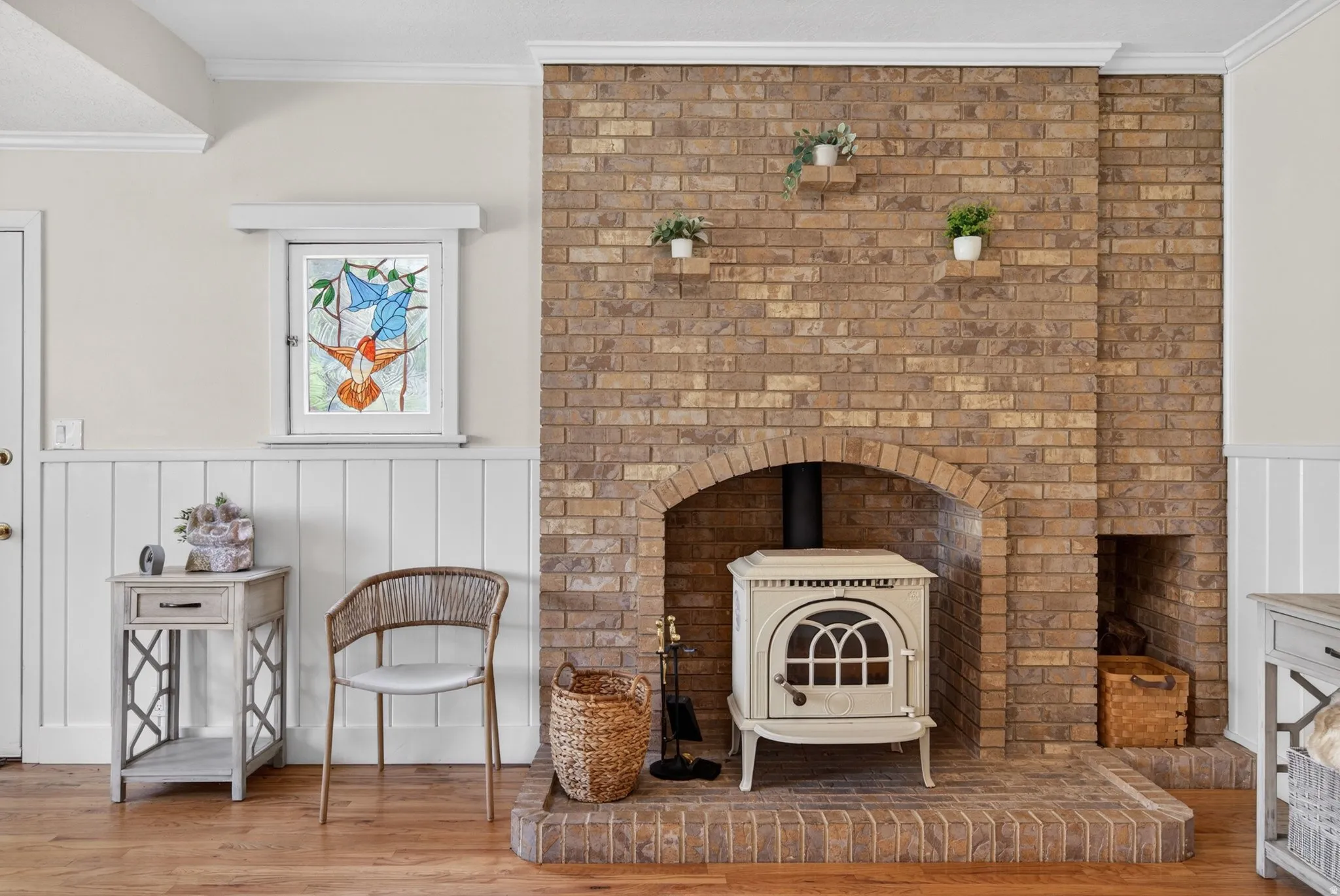 Living area with a wainscoted wall, a wood stove, crown molding, light wood finished floors, and a decorative wall