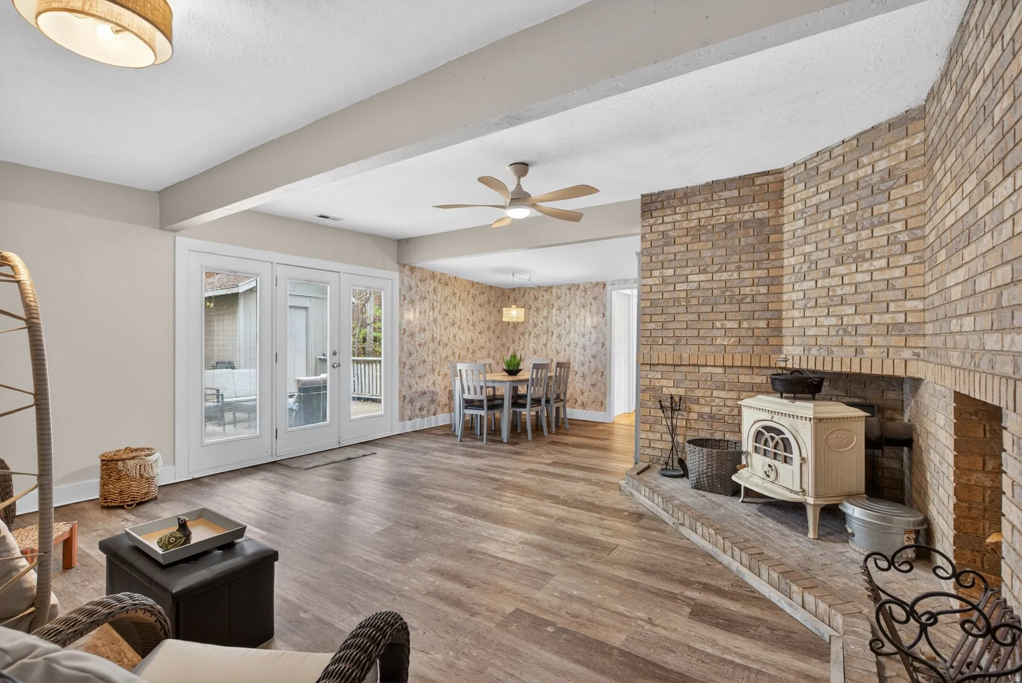Living area with wood finished floors, a wood stove, ceiling fan, a textured ceiling, and beamed ceiling
