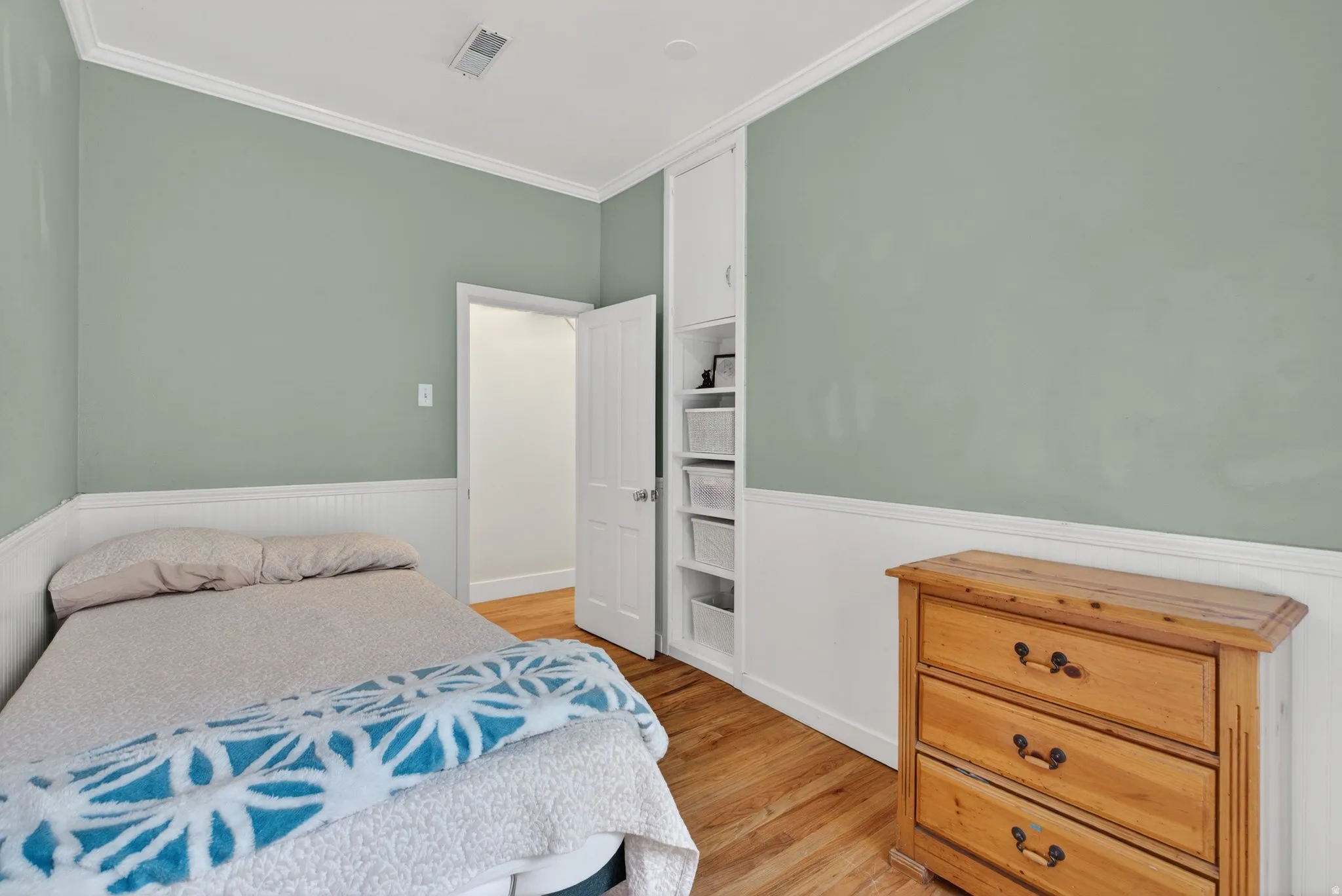 Bedroom with a wainscoted wall, light wood-type flooring, and crown molding