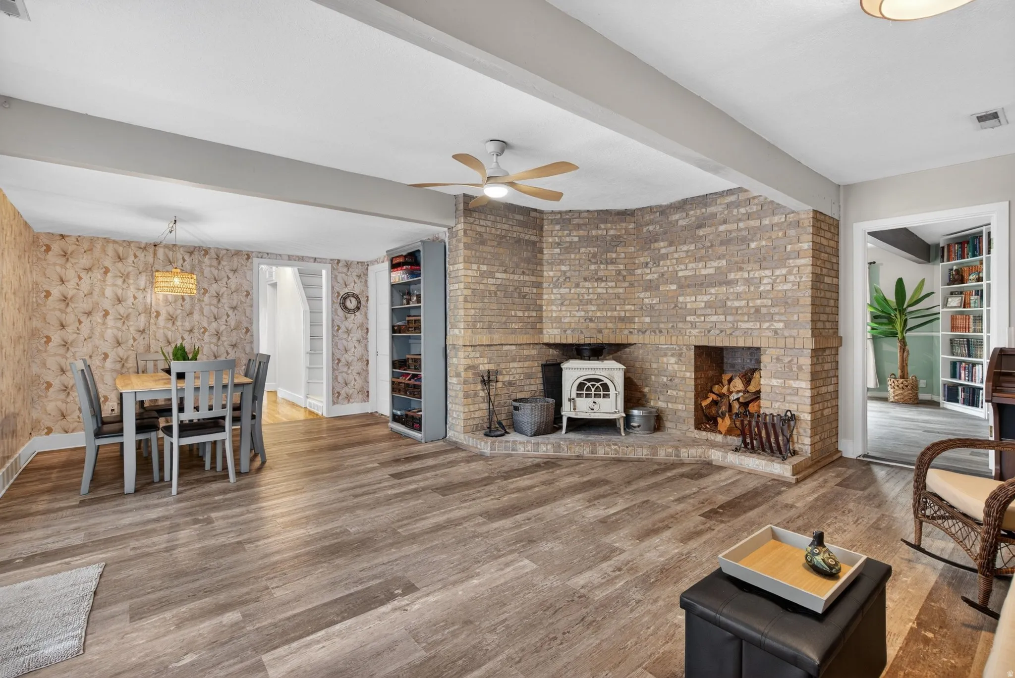 Living area with beamed ceiling, a ceiling fan, wood finished floors, a wood stove, and built in shelves