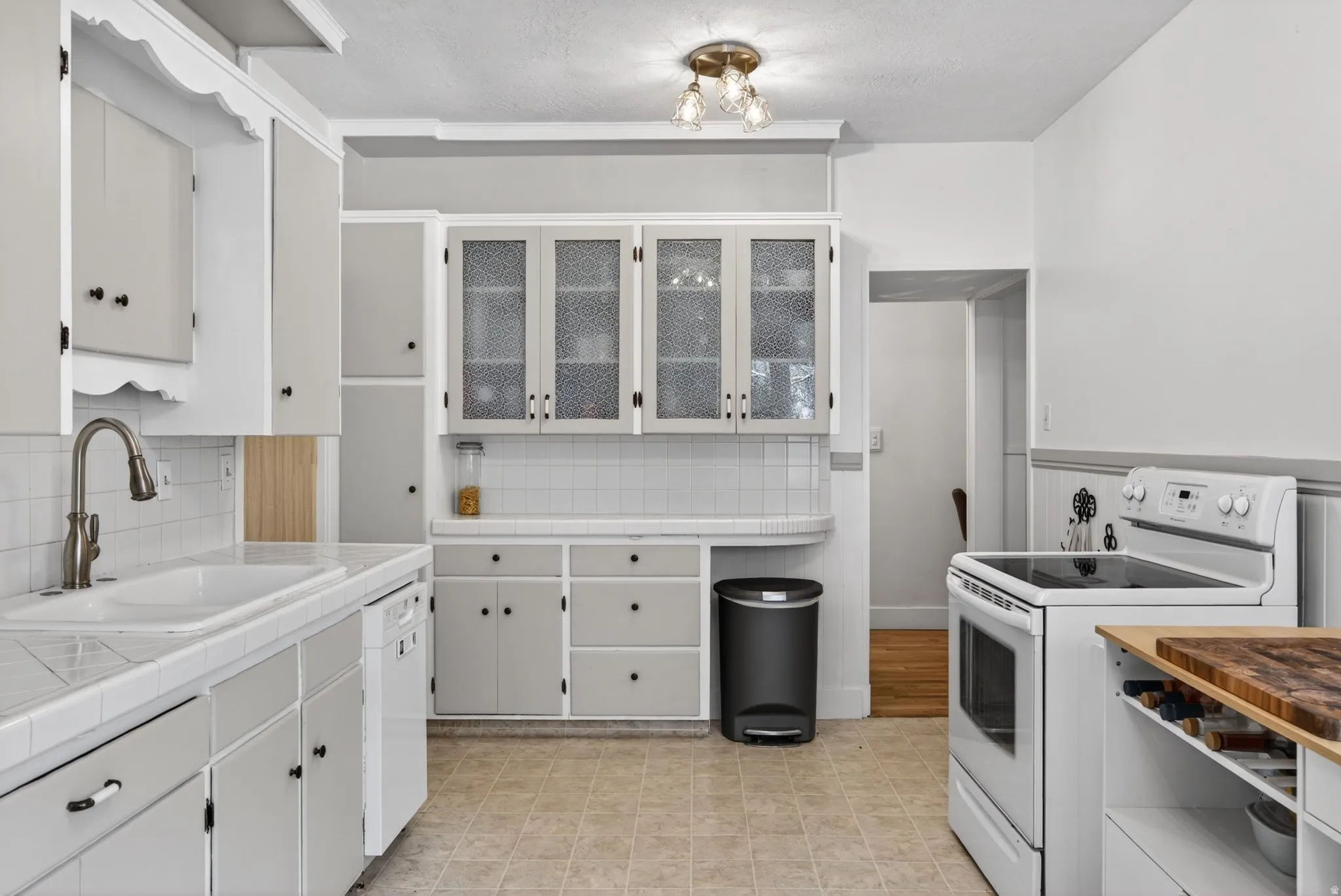 Kitchen featuring tile counters, white appliances, white cabinets, decorative backsplash, and wainscoting