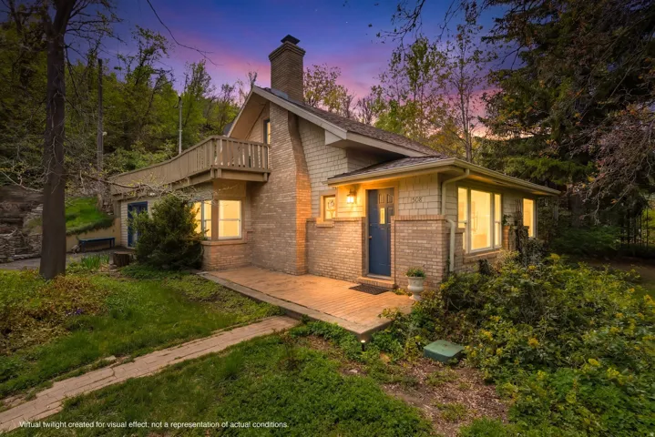 Back of property at dusk with brick siding, a deck, a chimney, and a balcony