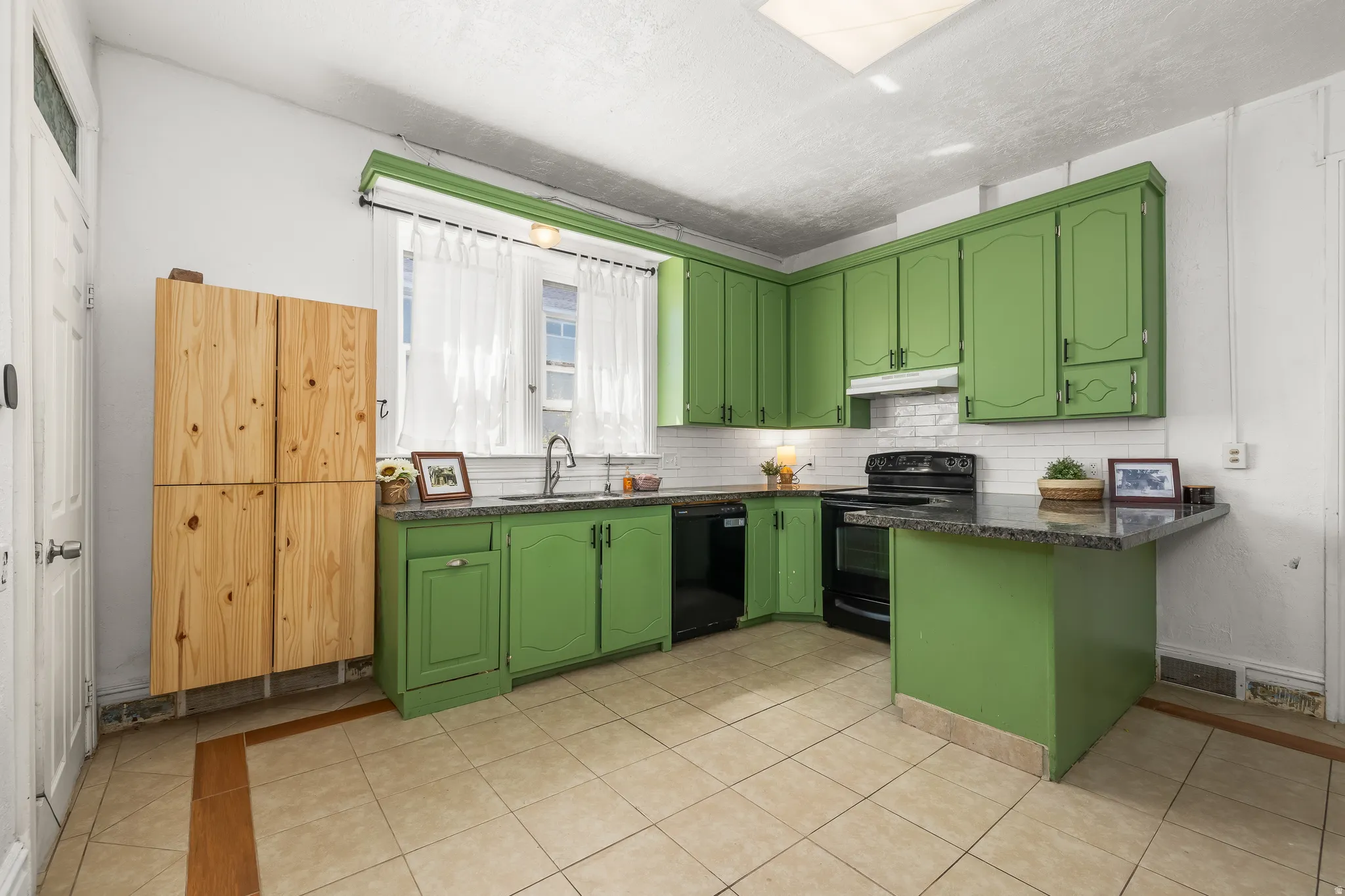 Kitchen featuring green cabinetry, a peninsula, black appliances, a kitchen breakfast bar, and light tile patterned floors