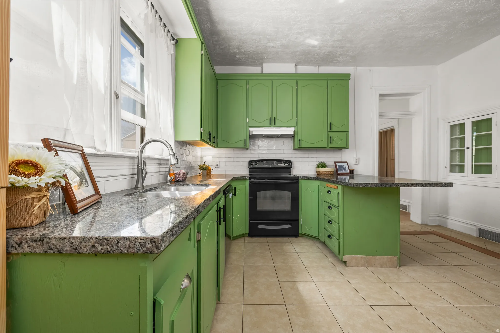 Kitchen featuring green cabinetry, electric range, a peninsula, dark stone countertops, and a breakfast bar