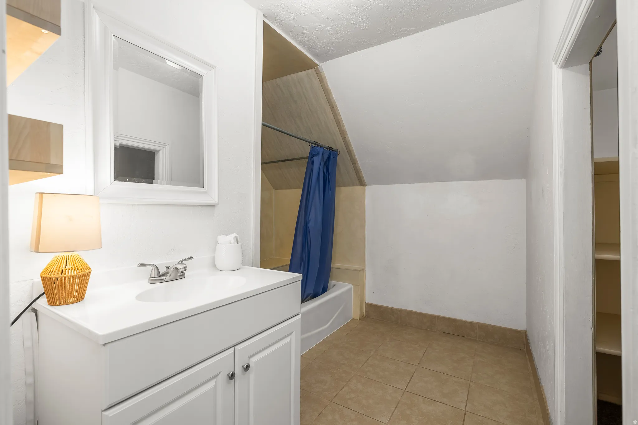 Full bath featuring vanity, lofted ceiling, shower / bath combination with curtain, and light tile patterned floors