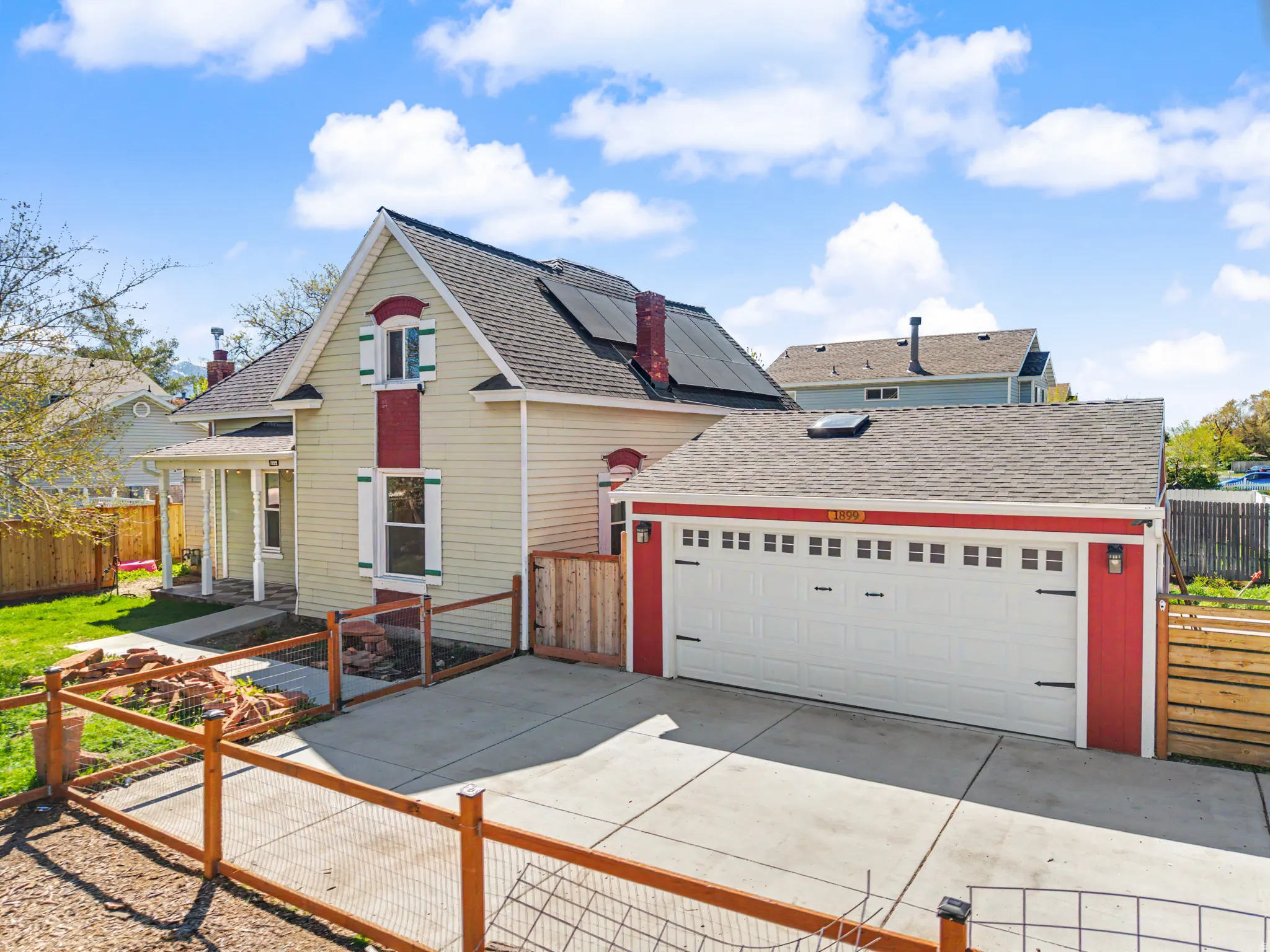 View of front of property with a fenced front yard, roof with shingles, a garage, roof mounted solar panels, and driveway