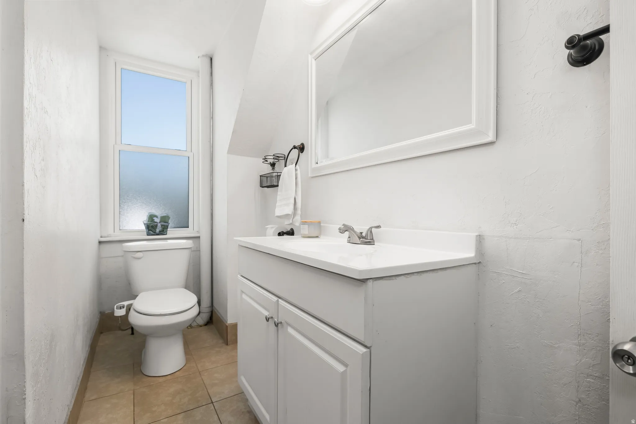Bathroom featuring vanity, lofted ceiling, light tile patterned floors, and a textured wall