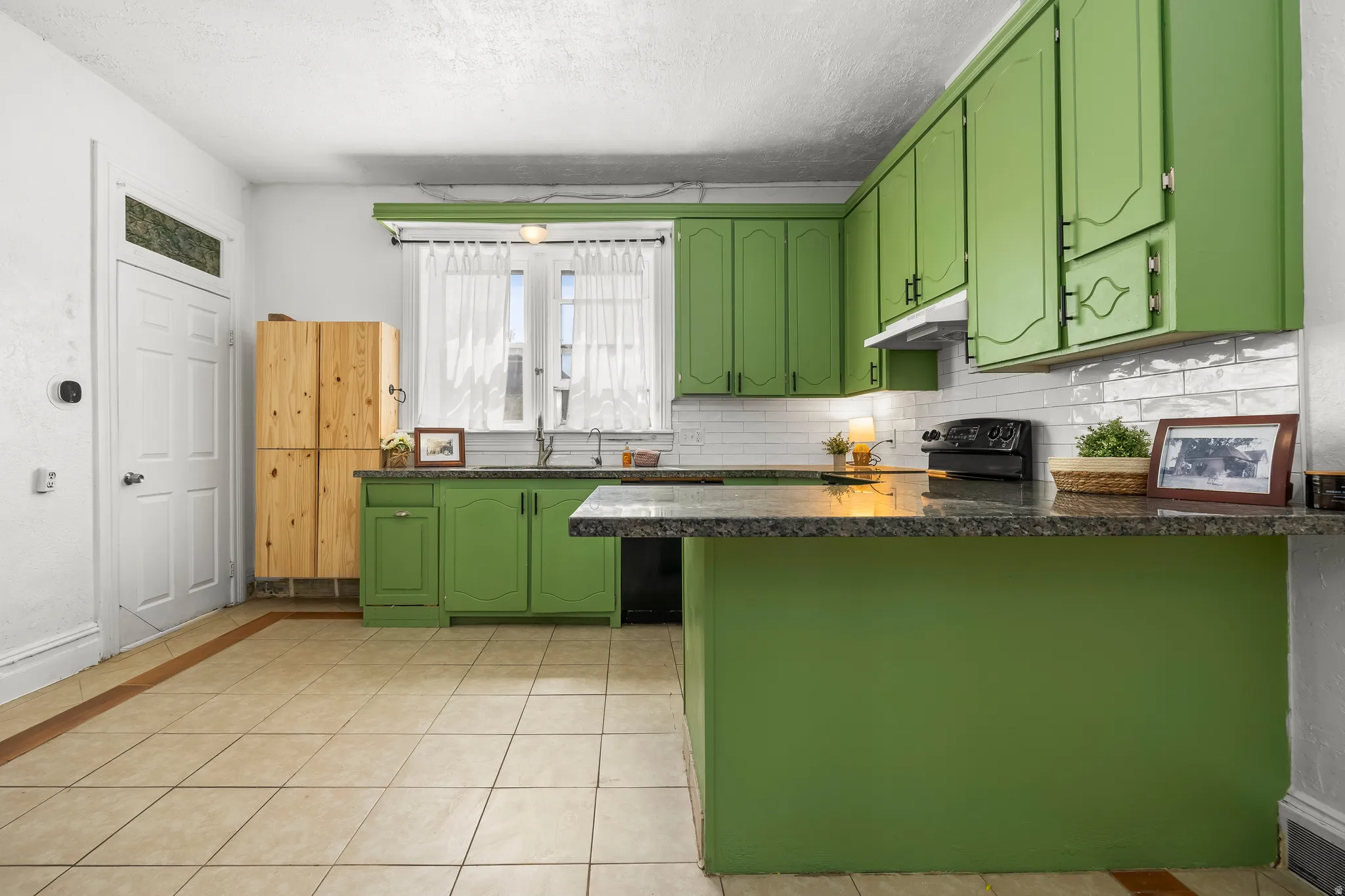Kitchen featuring green cabinets, a peninsula, black appliances, light tile patterned floors, and dark stone counters