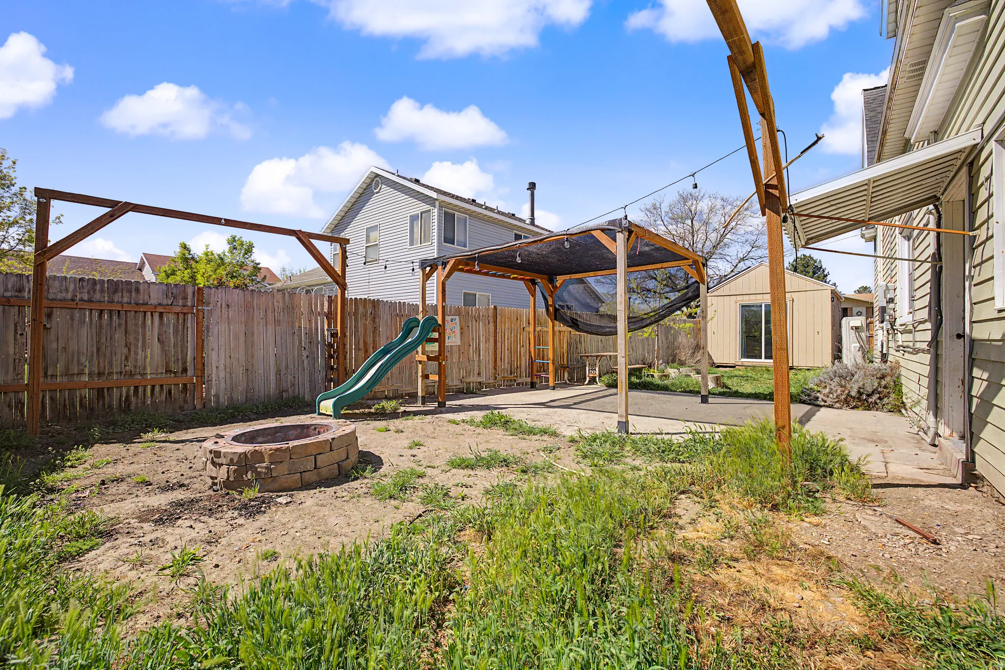 Fenced backyard featuring a patio area, a fire pit, a shed, a playground, and a gazebo