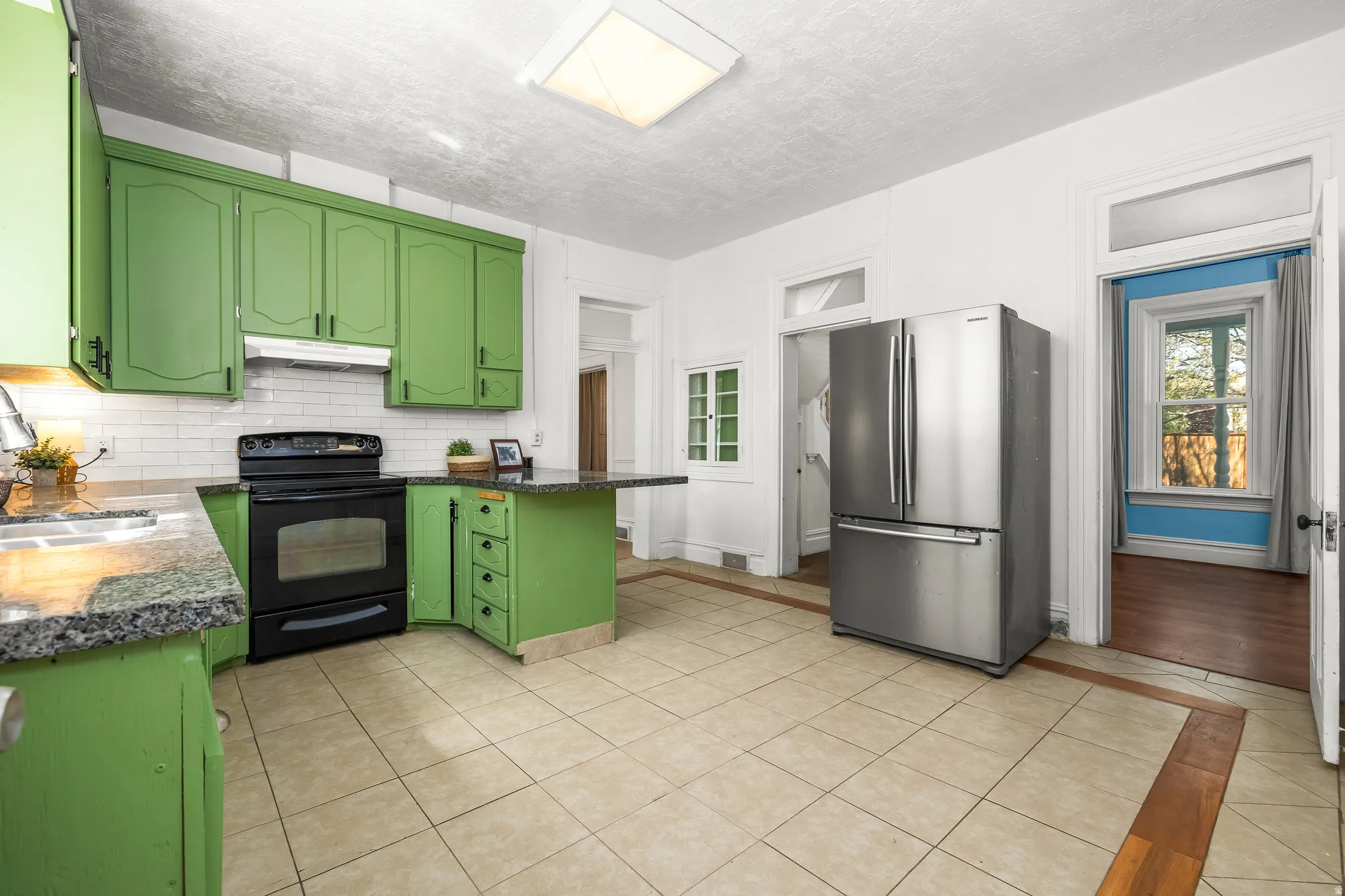 Kitchen featuring green cabinetry, freestanding refrigerator, black electric range, light tile patterned floors, and dark stone counters