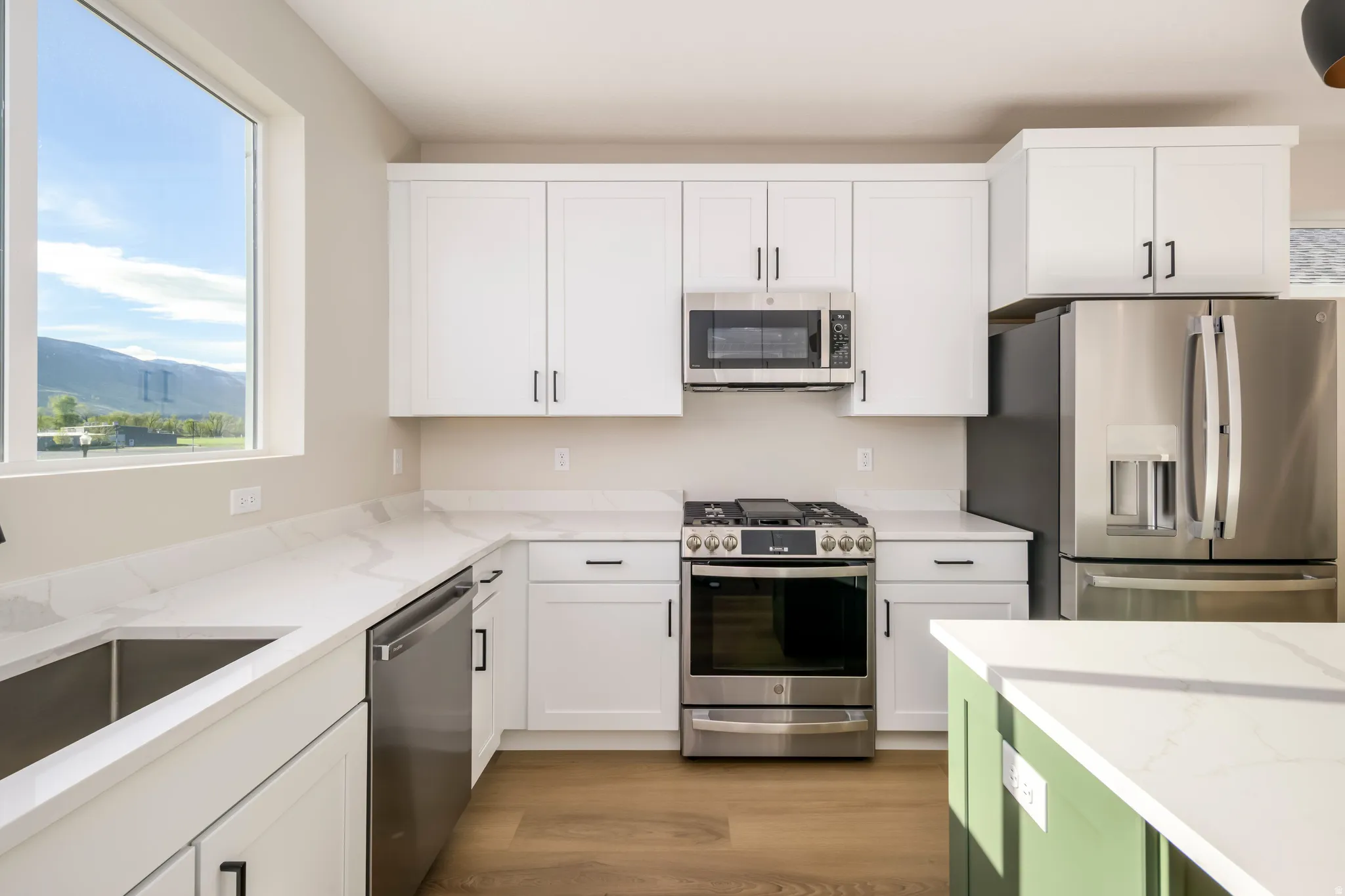 Two tone kitchen with stainless steel appliances, light stone countertops, light wood finished floors, a mountain view, and two tone color scheme