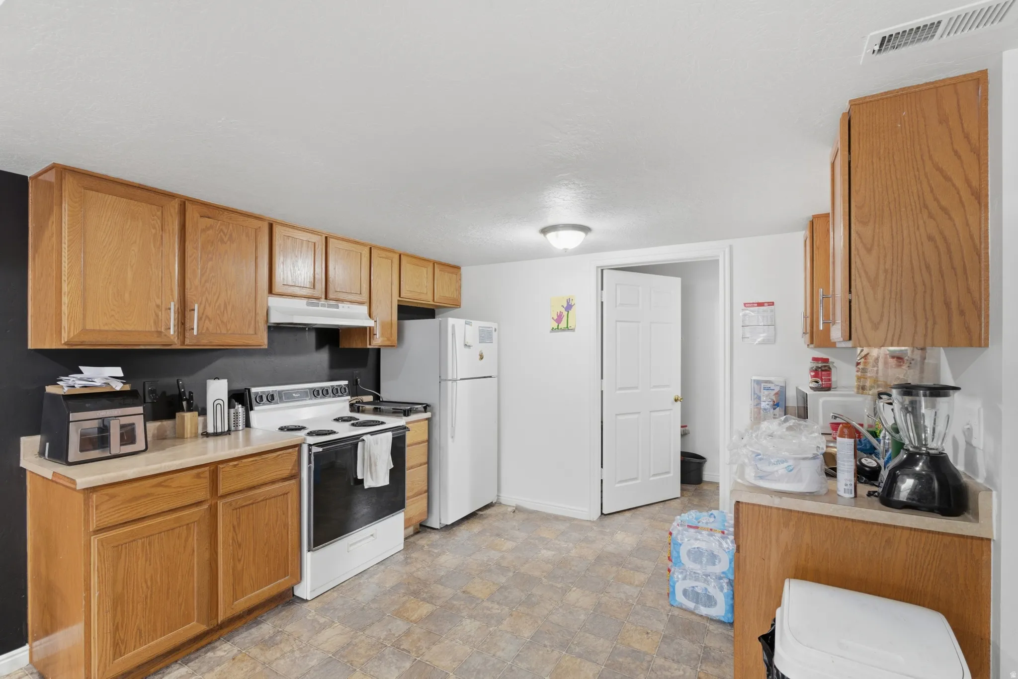 Kitchen featuring white appliances, light countertops, stone finish flooring, and wood finish cabinets