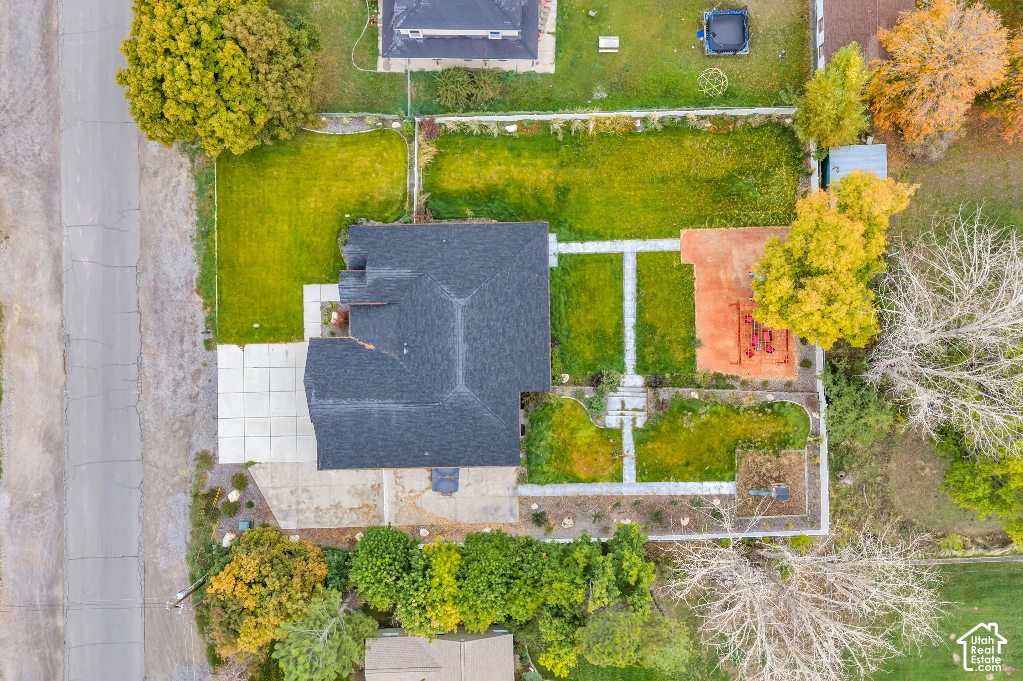 Aerial perspective featuring a multi-tiered lot with stone-paver walkways, a concrete driveway, mature trees, and perimeter fencing