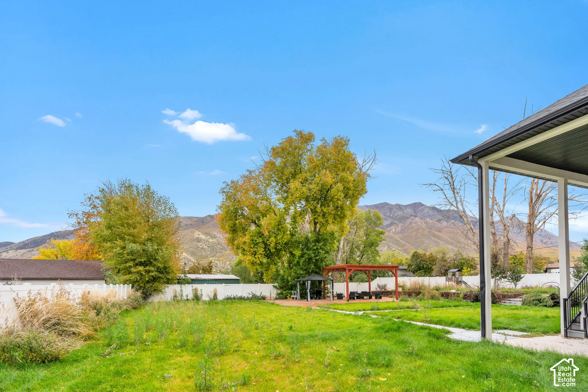 Expansive backyard featuring a covered patio, wooden pergola, white privacy fencing, and mountain backdrop