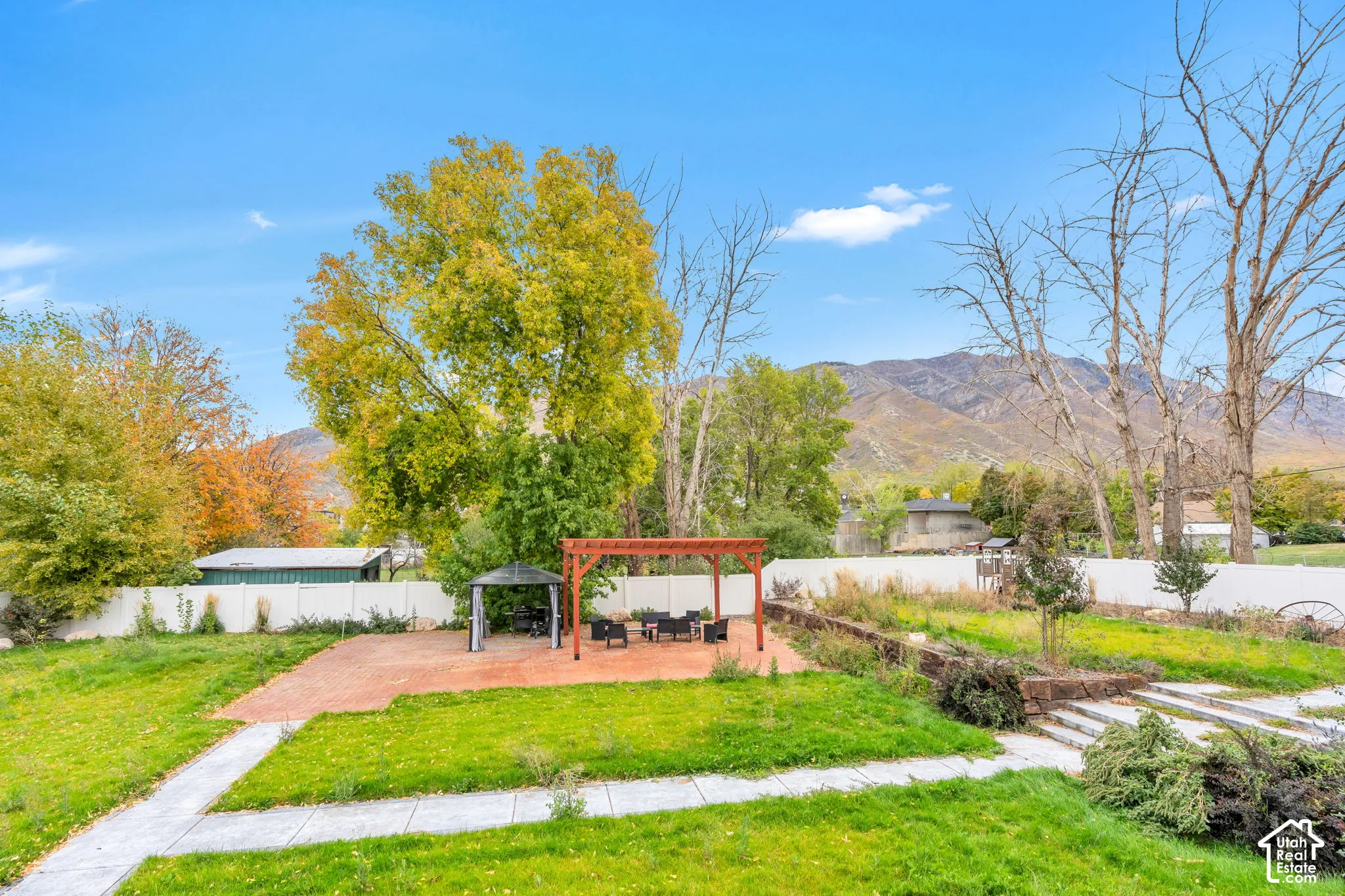 Backyard featuring a brick patio, wooden pergola, tiered stone retaining wall, concrete walkways, and mountain backdrop