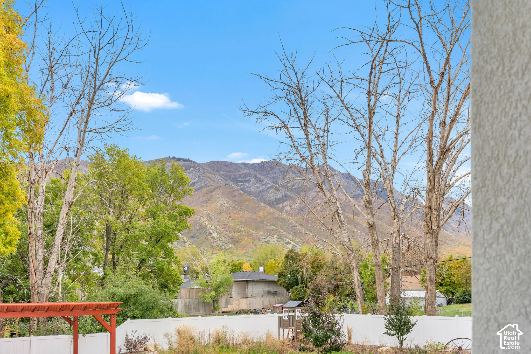 Exterior space featuring a mountain backdrop, mature trees, and a white privacy fence