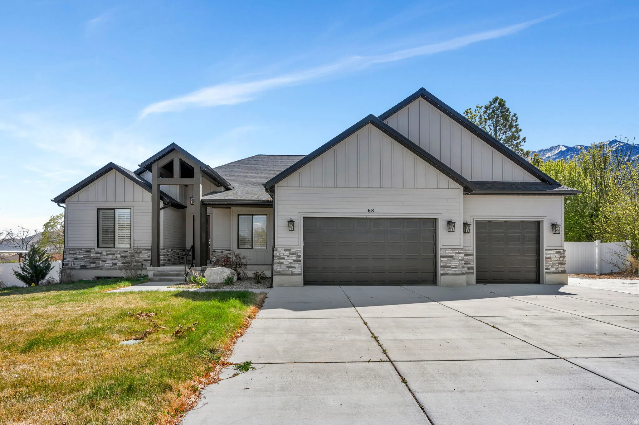Modern farmhouse featuring board and batten siding, stone siding, a garage, a front lawn, and driveway