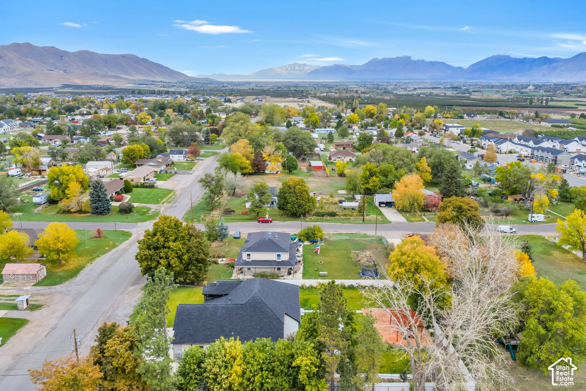 Aerial perspective featuring multi-story residential structures, mature deciduous trees, asphalt roadways, and an expansive mountain range backdrop