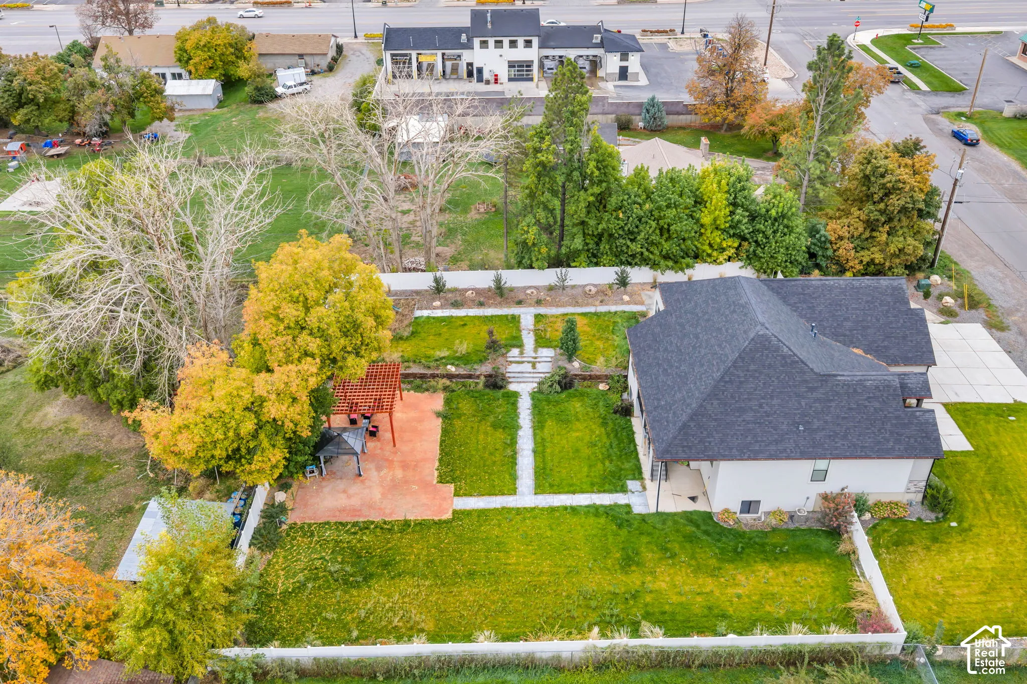 Expansive backyard featuring a stone-paved patio, a red wood-finish pergola, tiered garden areas, stone walkways, and mature landscaping