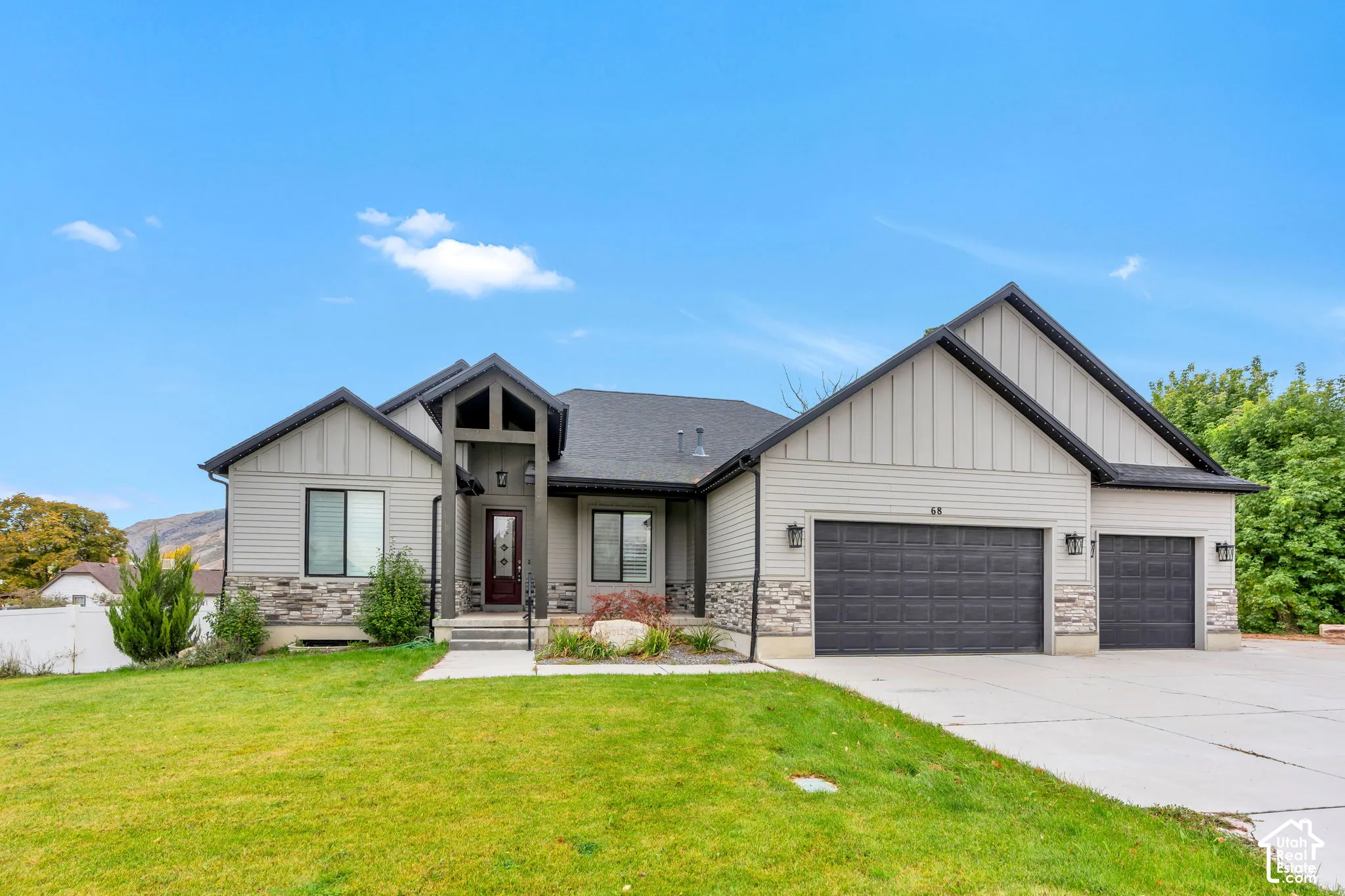 Single-level exterior featuring vertical board-and-batten siding, stone masonry accents, a three-car garage, and a covered front entryway