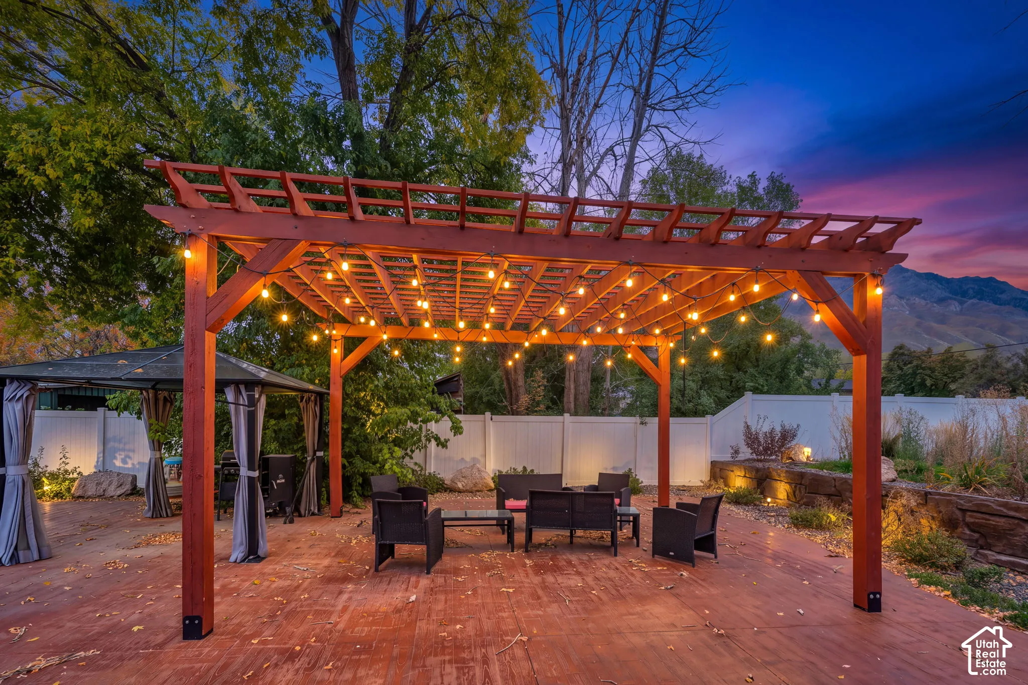 Stained-wood pergola featuring a lattice roof, paved patio surface, white vinyl privacy fencing, and stone retaining wall