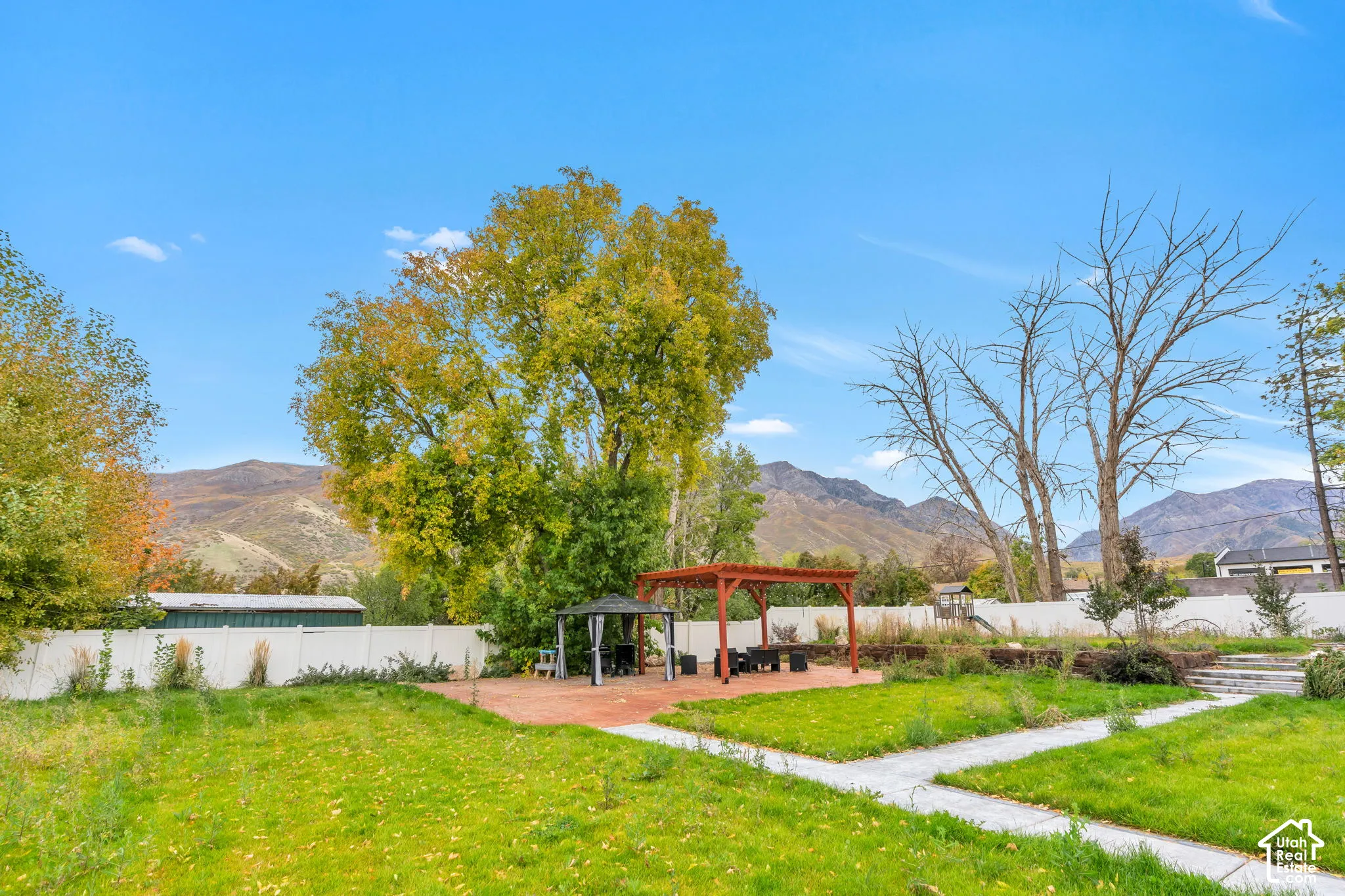 Expansive backyard featuring a brick paver patio, wood pergola, covered gazebo, and mountain backdrop