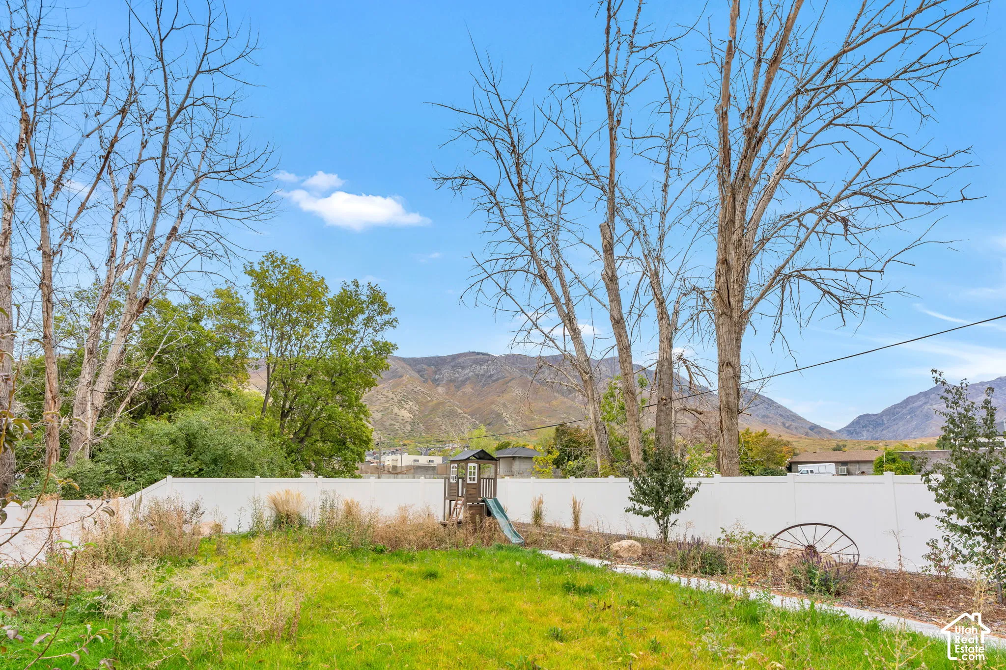 Backyard featuring a white vinyl privacy fence, mature trees, and a mountain backdrop