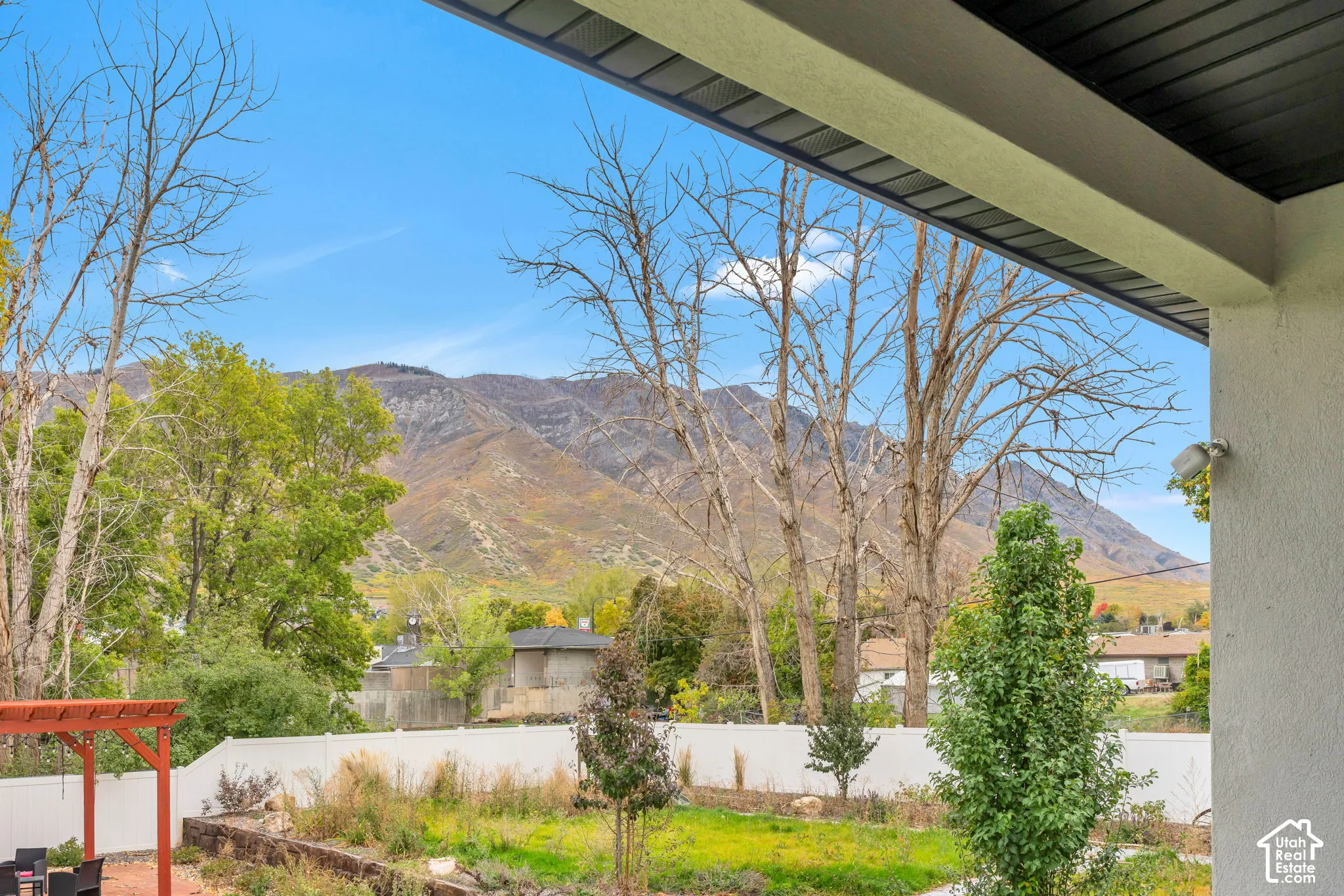 Covered patio with a dark-finished ceiling, white vinyl fencing, and a red-toned pergola, featuring mountainous scenery