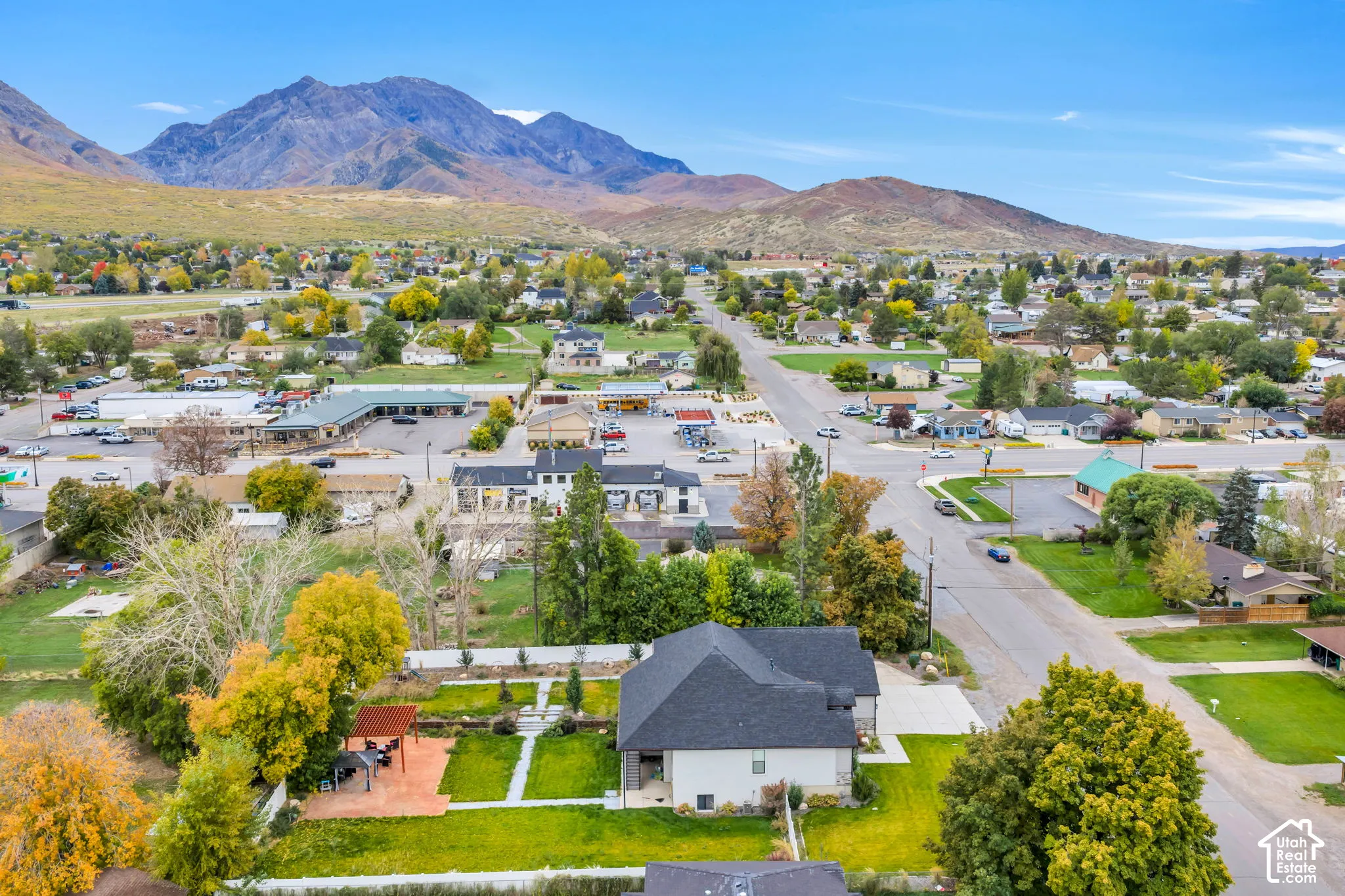 Aerial perspective featuring a multi-level residential structure with a shingled roof, a paved patio, and established trees set against a mountain backdrop